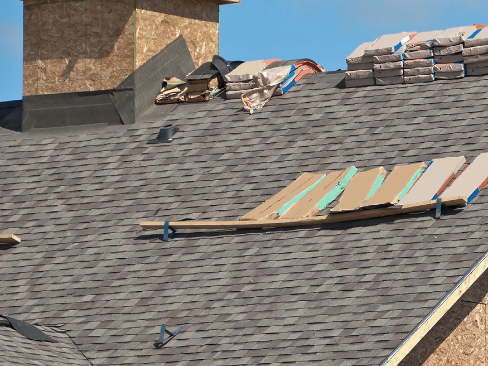 New roof installation with asphalt shingles, roofing materials, and chimney under construction on sunny day.