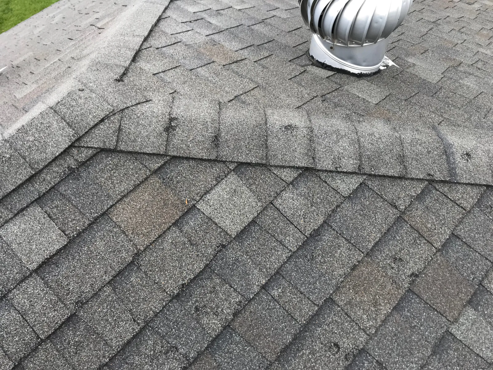 Close-up of gray asphalt shingles with a metal roof vent on a residential roof.