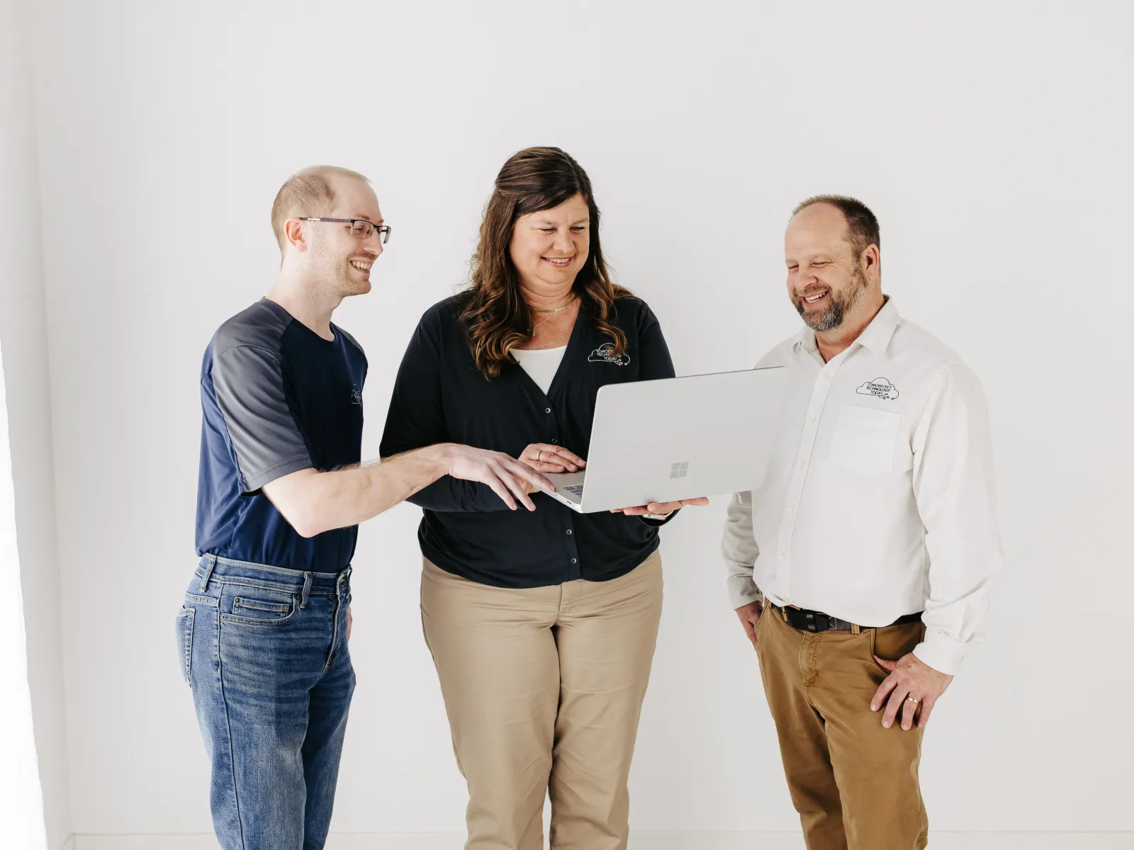 Three colleagues standing and looking at a laptop, smiling and discussing in a bright office space