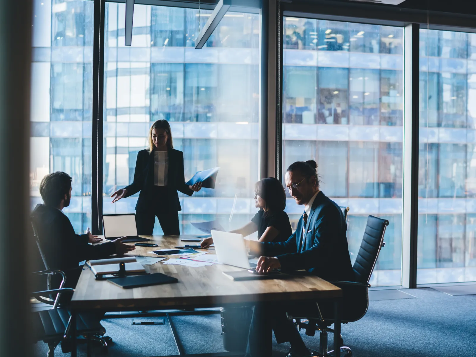 Business team in a modern office meeting with large windows and cityscape views discussing work.