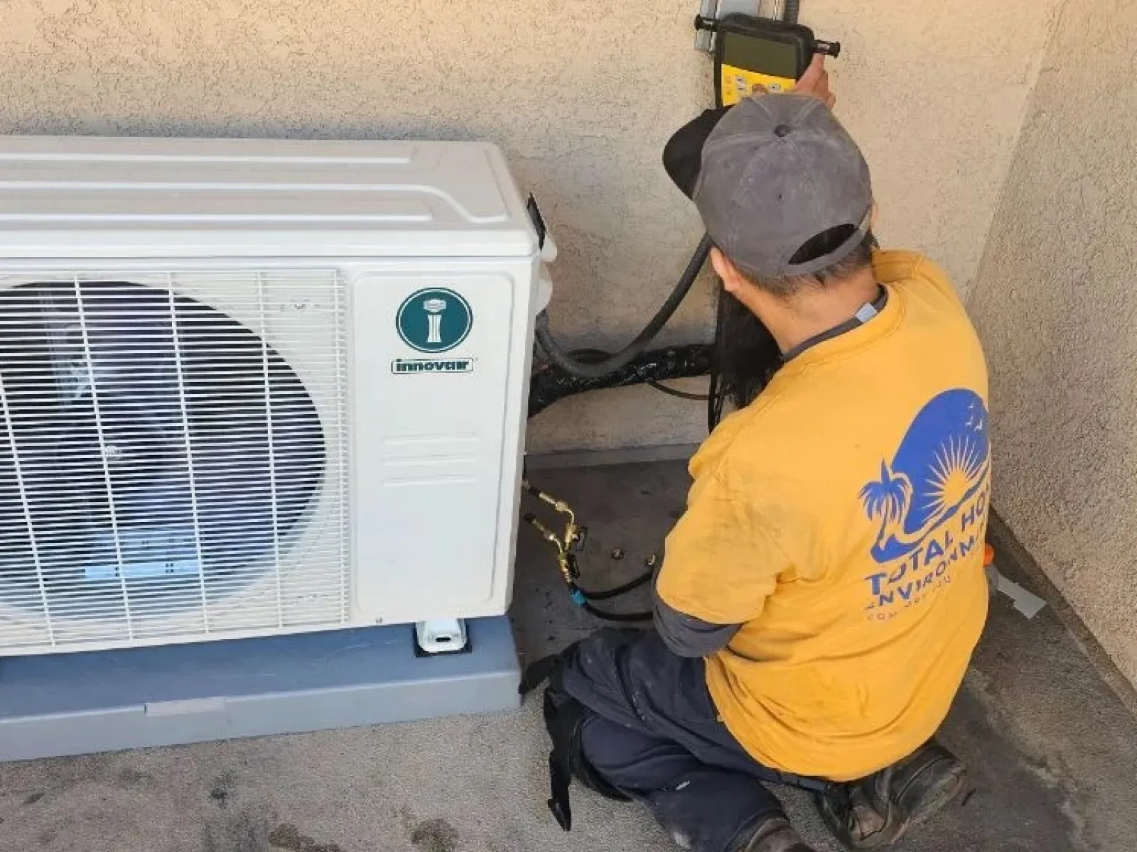 Technician installing or repairing an outdoor air conditioning unit on a concrete surface near a stucco wall.