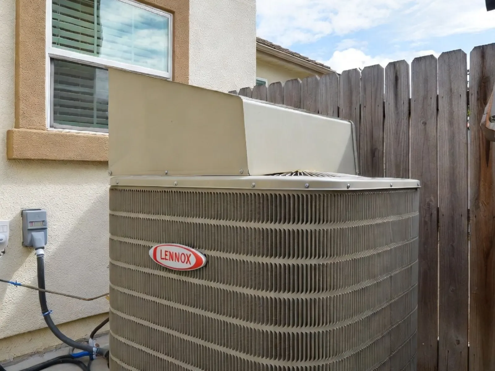 Outdoor Lennox air conditioning unit installed on concrete pad beside house with wooden fence.