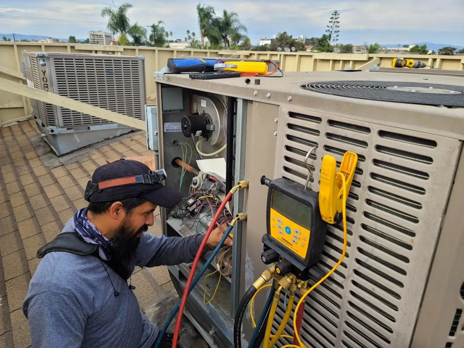 Technician inspecting and repairing rooftop HVAC unit with diagnostic tools and gauges during maintenance work.