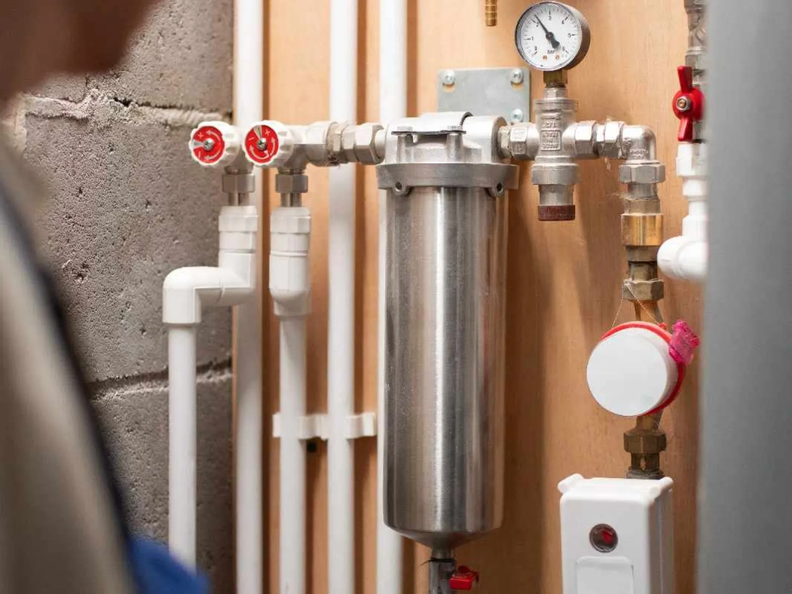 Man inspecting a complex water filtration system with pipes, gauges, and valves mounted on a wooden wall.
