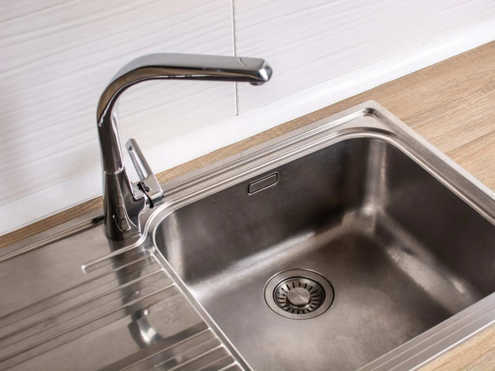 Modern kitchen sink with tall chrome faucet and white tiled wall with hanging black utensils