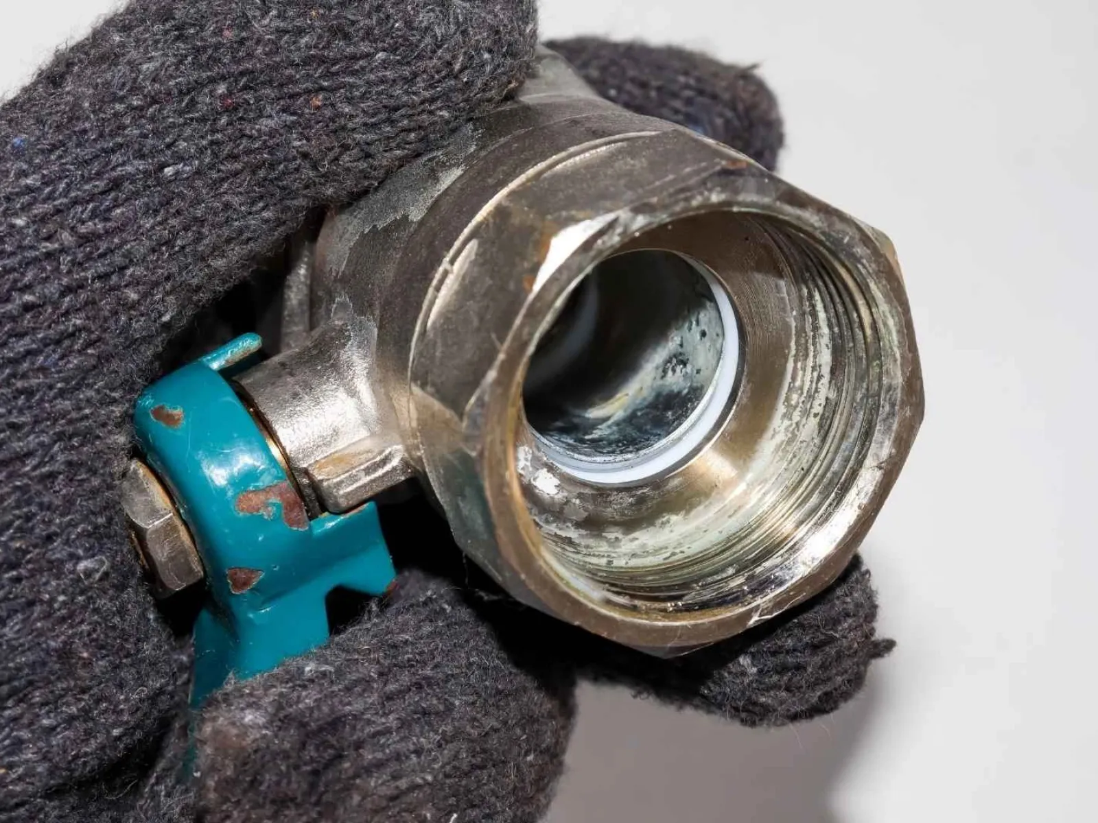 Close-up of a gloved hand holding a corroded metal valve with a blue handle against a white background