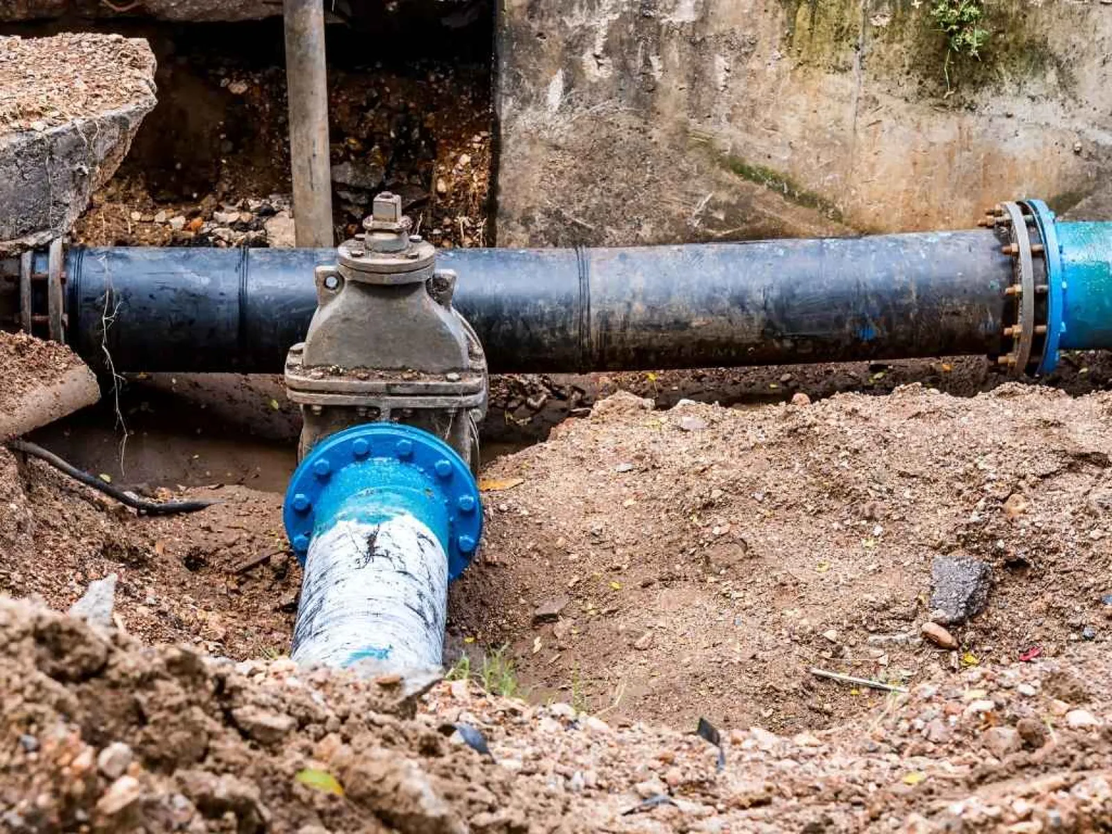 Construction site with exposed water pipes and valve surrounded by dirt and soil
