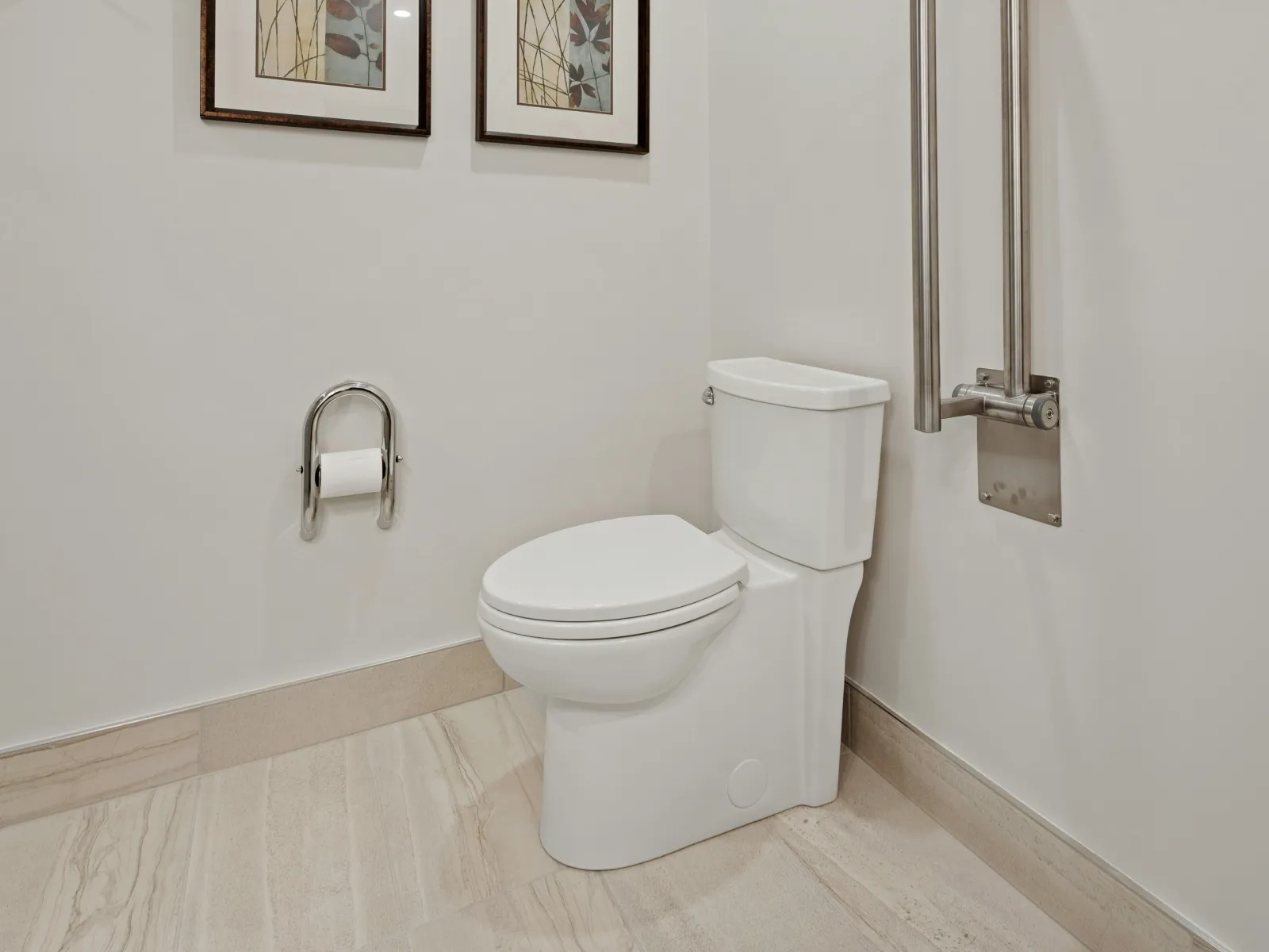Modern white toilet in a clean bathroom corner with beige tile flooring and framed wall art