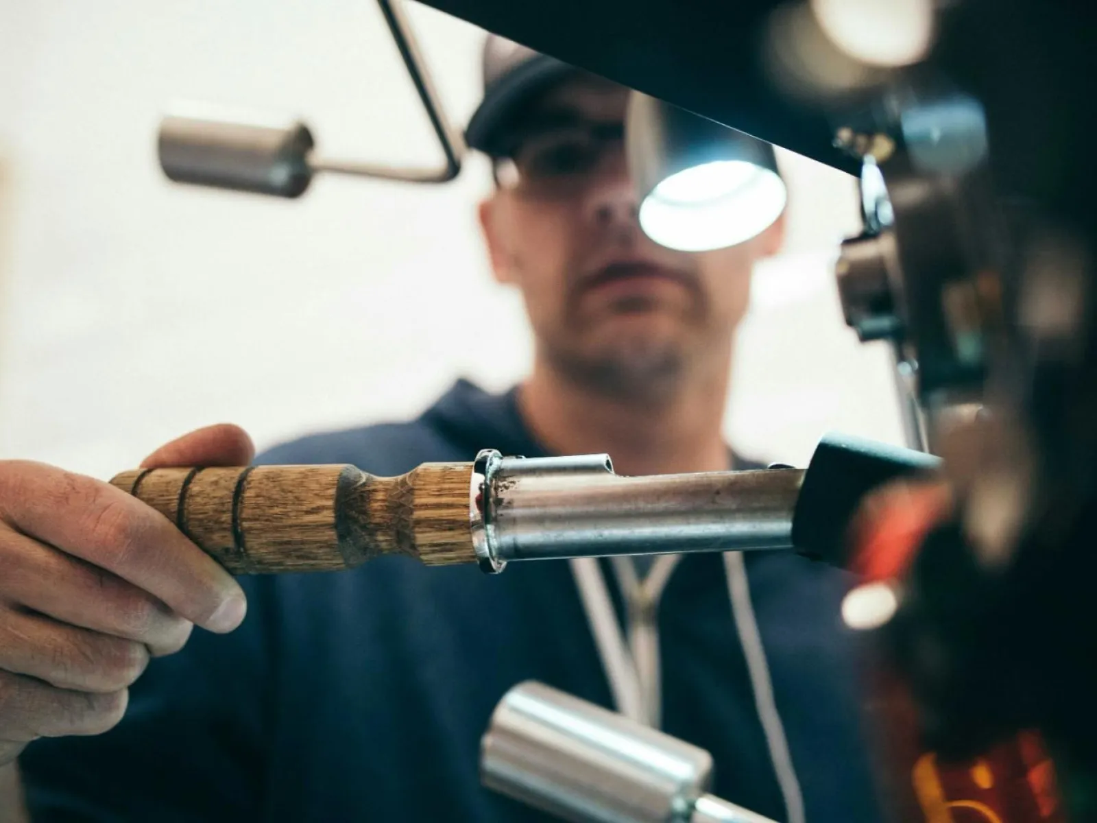Barista adjusting wooden handle on espresso machine in a coffee shop setting.