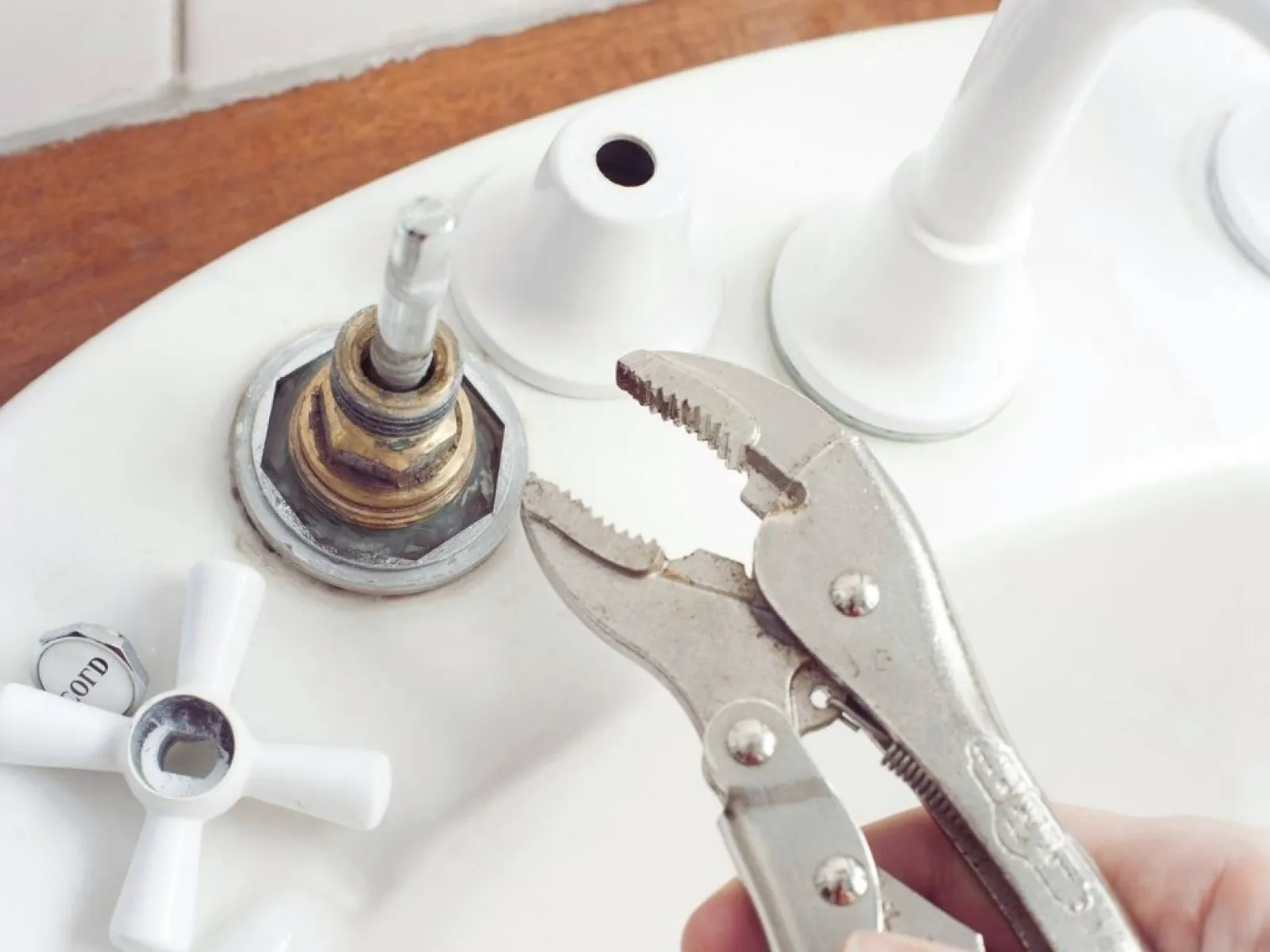 Close-up of a person using locking pliers to repair a bathroom sink faucet handle.
