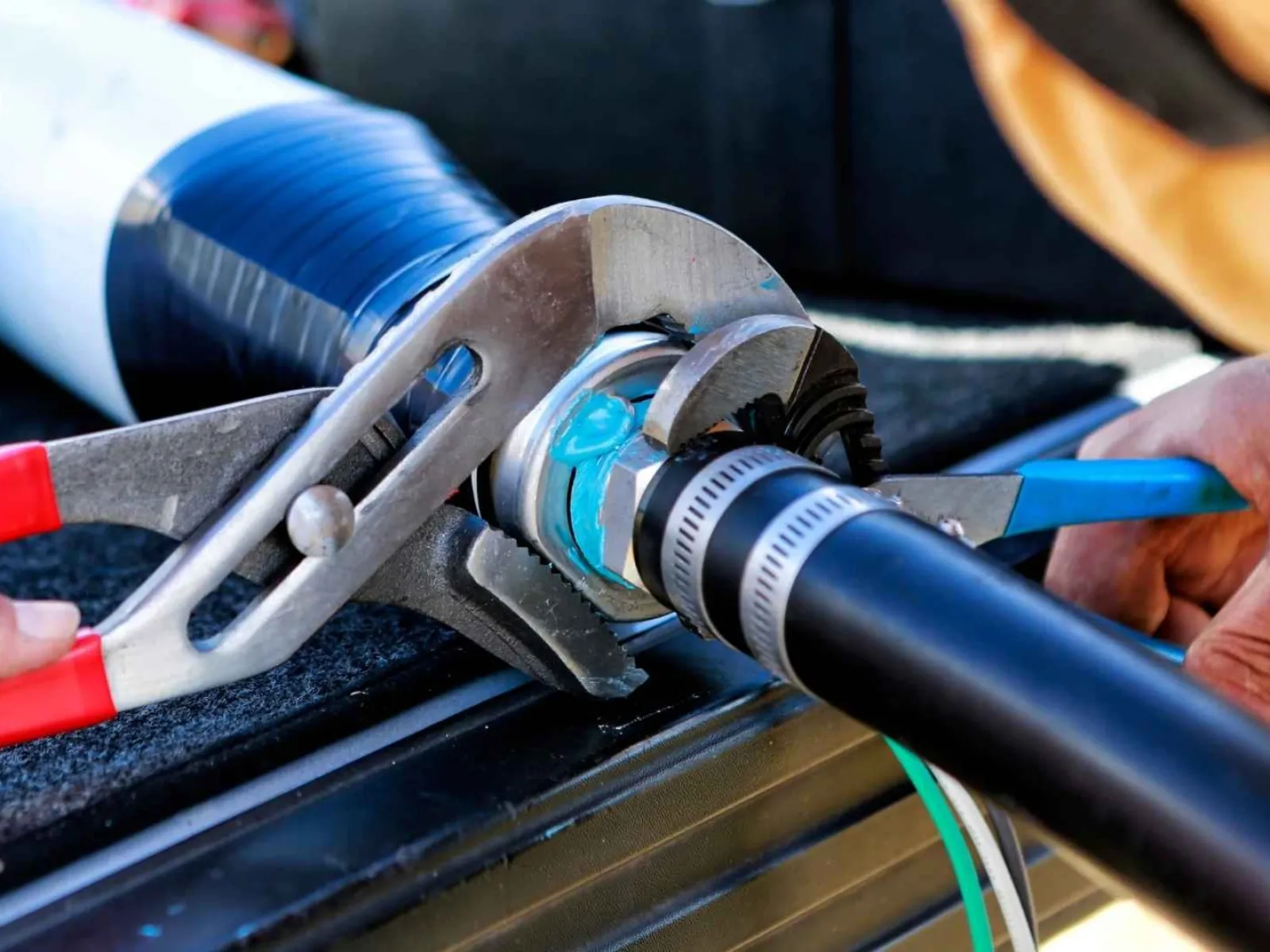 Hands using wrenches to secure a hose clamp on a black rubber tube connection outdoors.