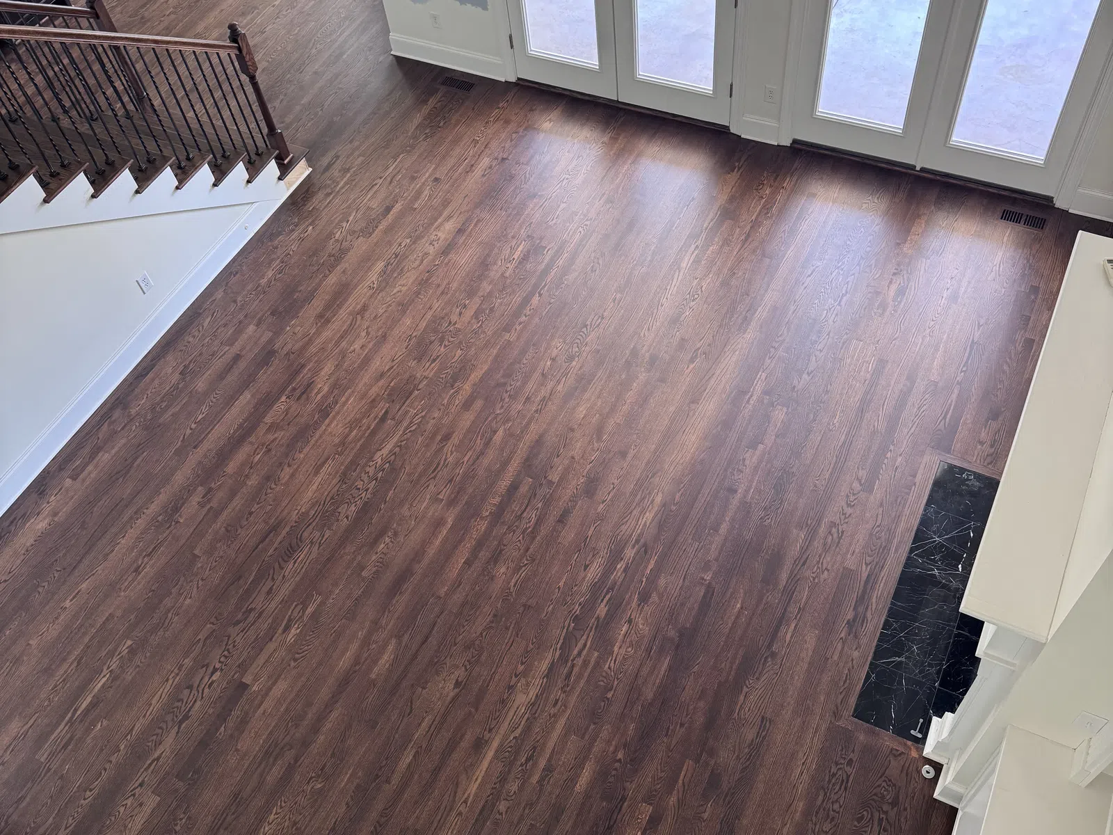 Spacious room with dark wooden floors, white walls, large glass doors, and a staircase with iron railing.
