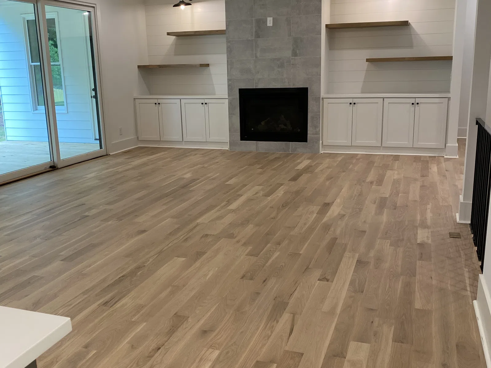 Modern living room with wood floors, gray tiled fireplace, white cabinets, open shelves, and large sliding door.