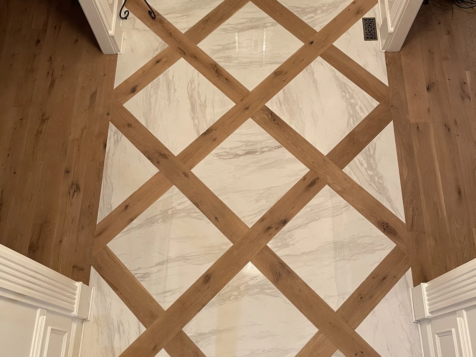 Modern entryway floor with crisscross wood and marble tile pattern in front of dark double doors