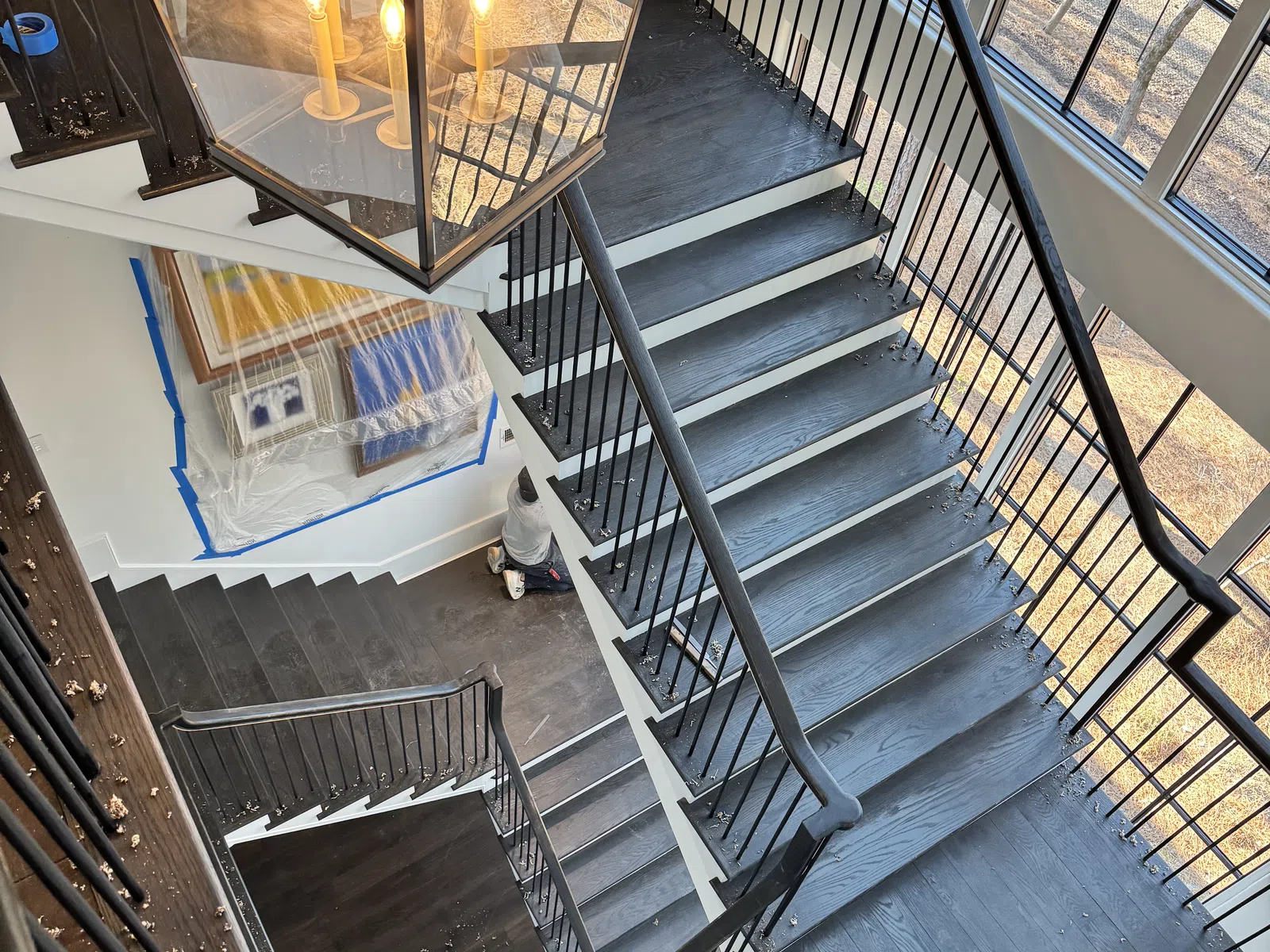 Overhead view of a multi-level modern staircase with black wood steps and metal railings under a large pendant light.
