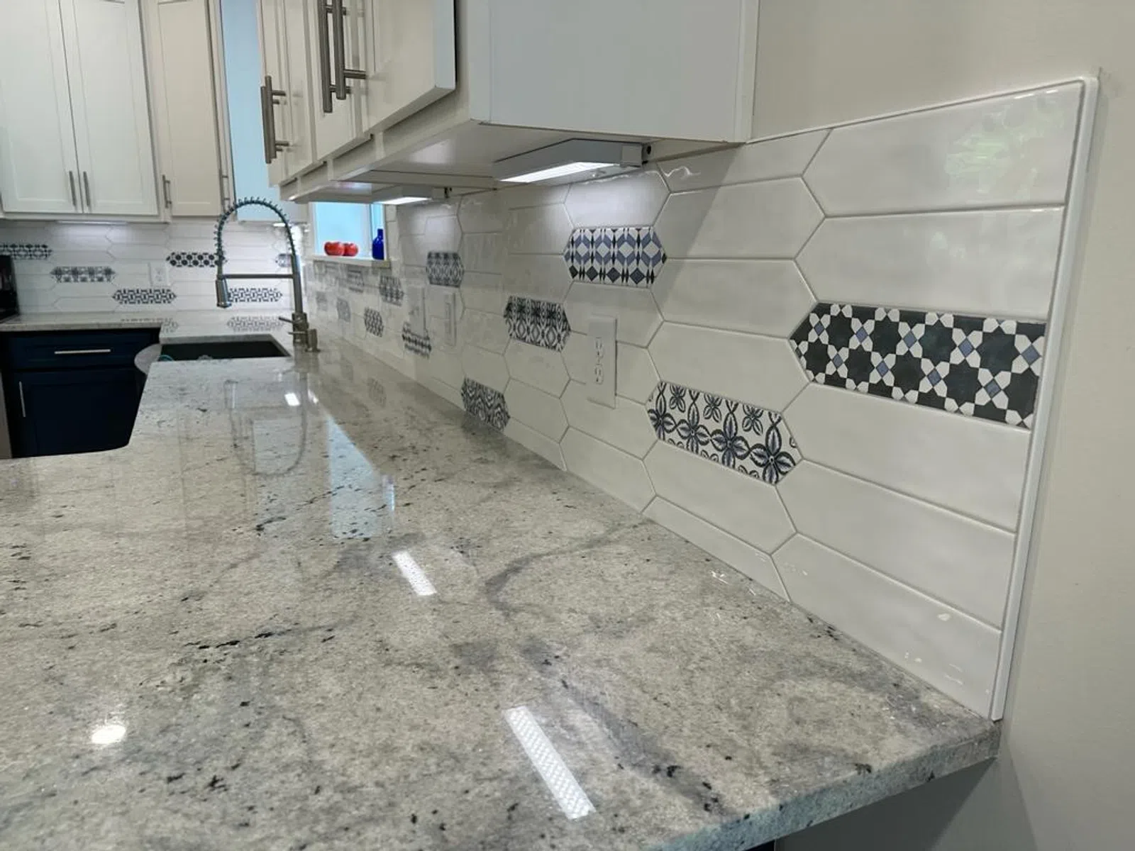 Modern kitchen countertop with polished granite and white hexagonal backsplash tiles with blue geometric patterns.
