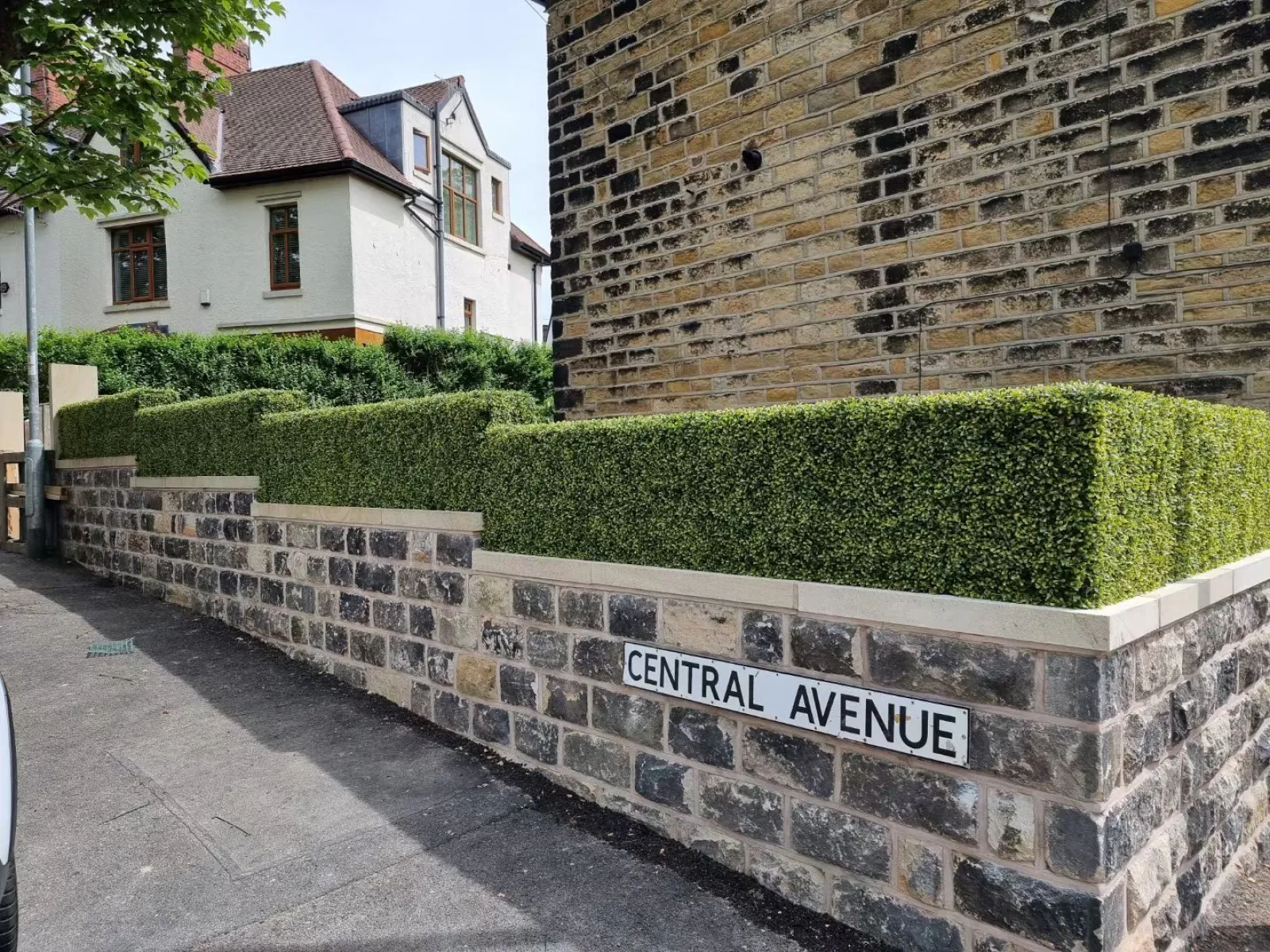 Stone wall with Central Avenue street sign and neatly trimmed hedge in front of residential buildings.