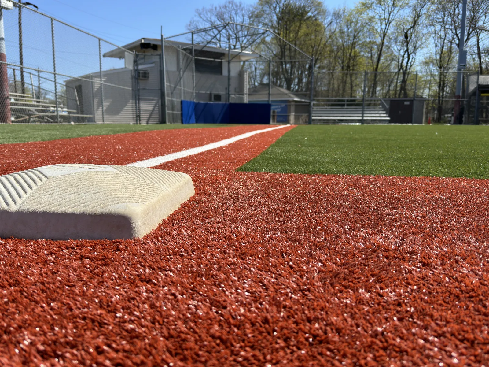 Close-up of first base on a sunlit baseball field with artificial turf and white foul line.