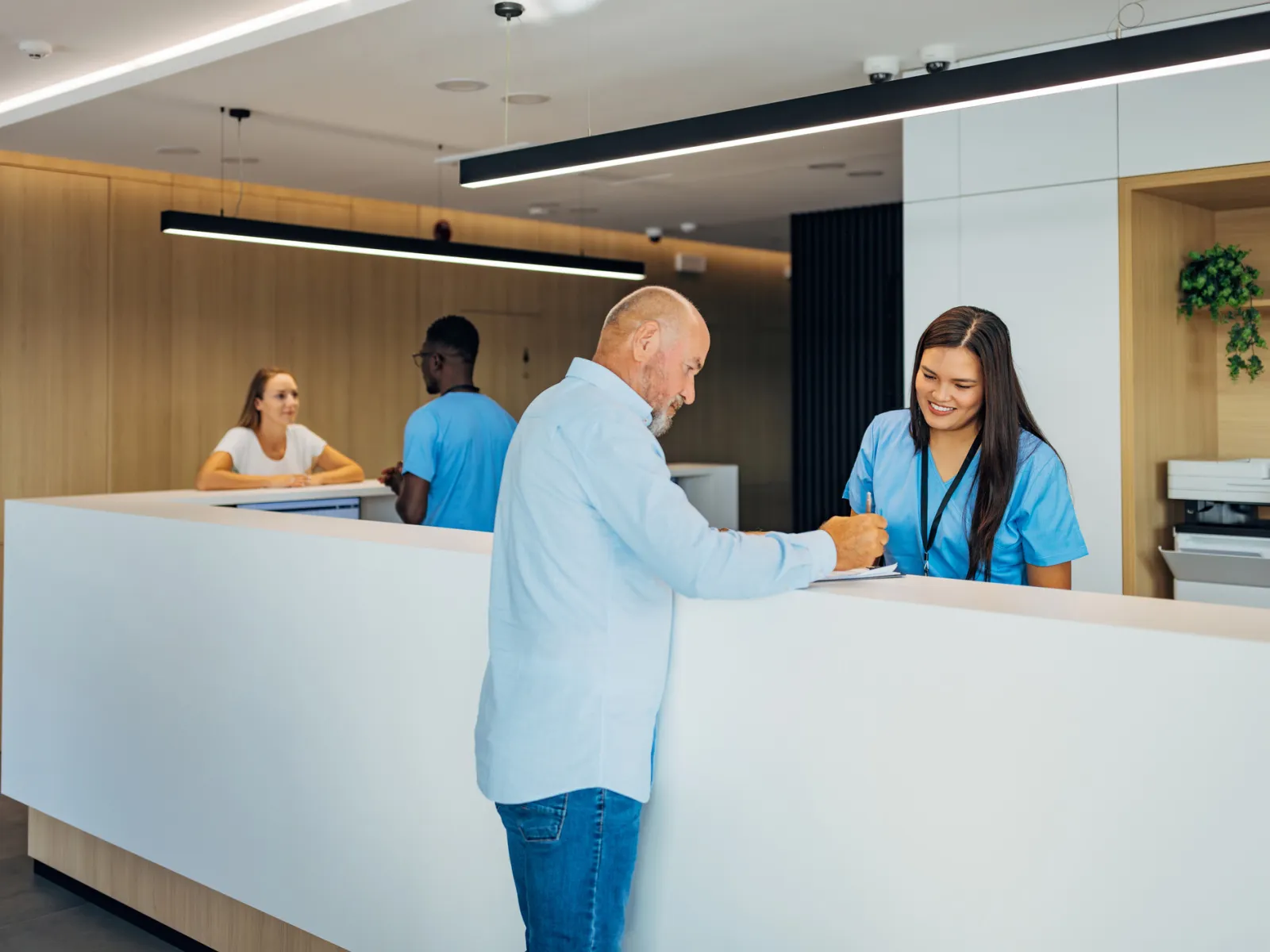 Patient signing forms at a modern medical clinic reception desk with healthcare staff assisting.