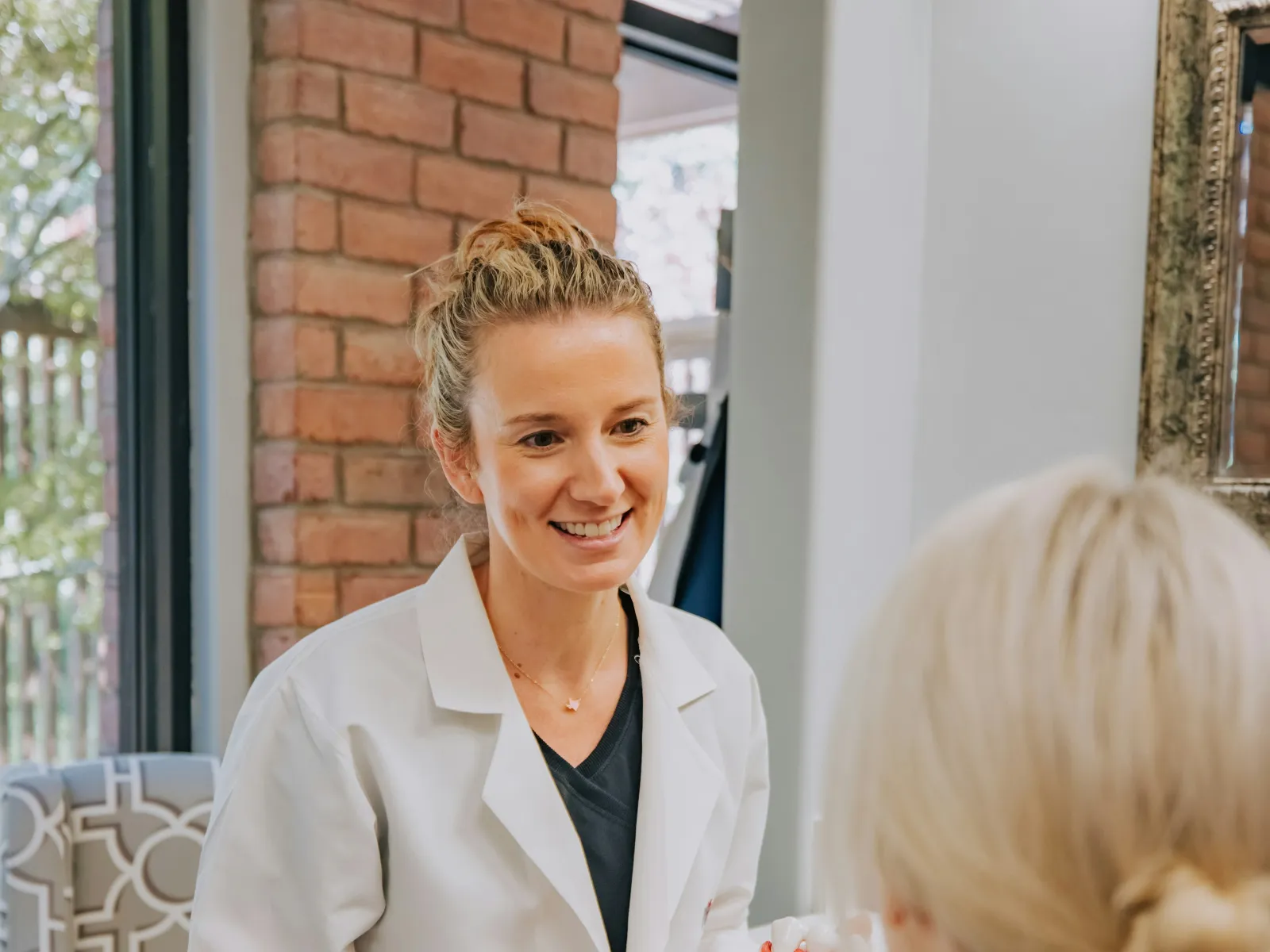 Dentist in white coat explaining a dental model to a patient in a modern office with brick wall background