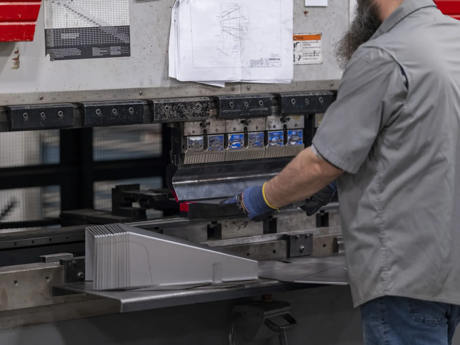 Worker operating a machine press to shape metal sheets in an industrial workshop environment
