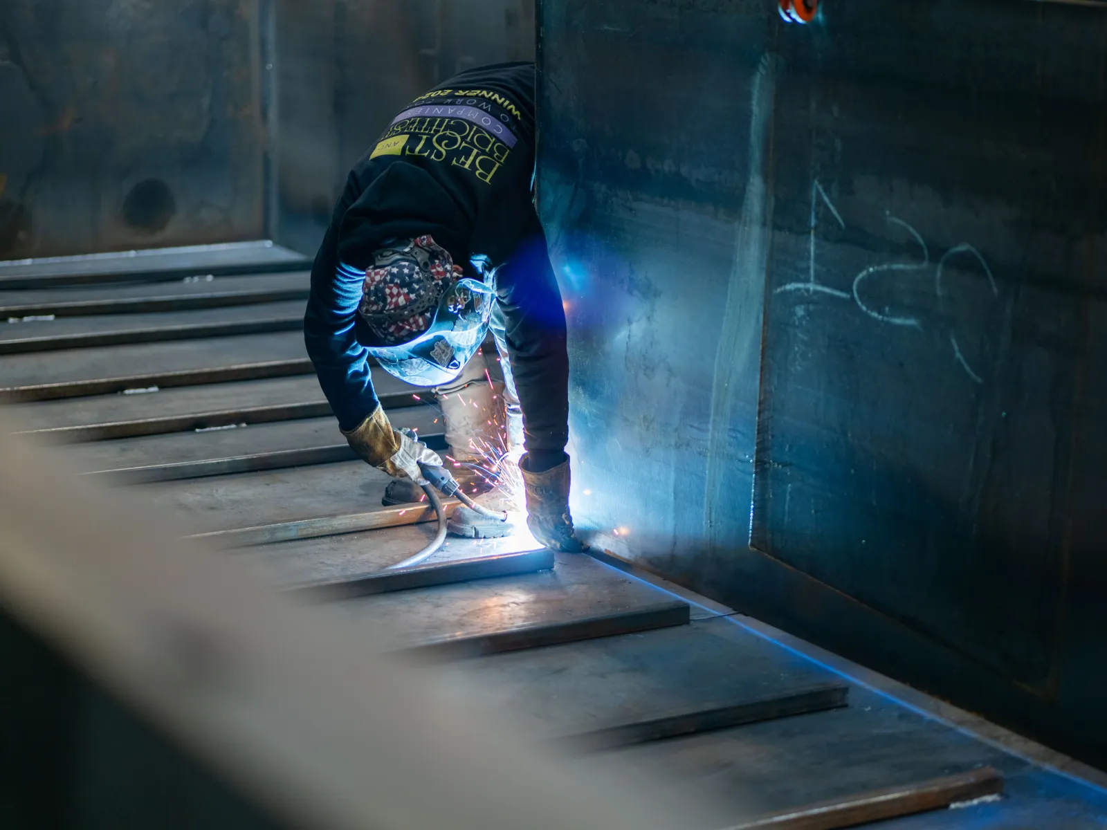 Welder in protective gear working on metal with sparks flying in an industrial setting