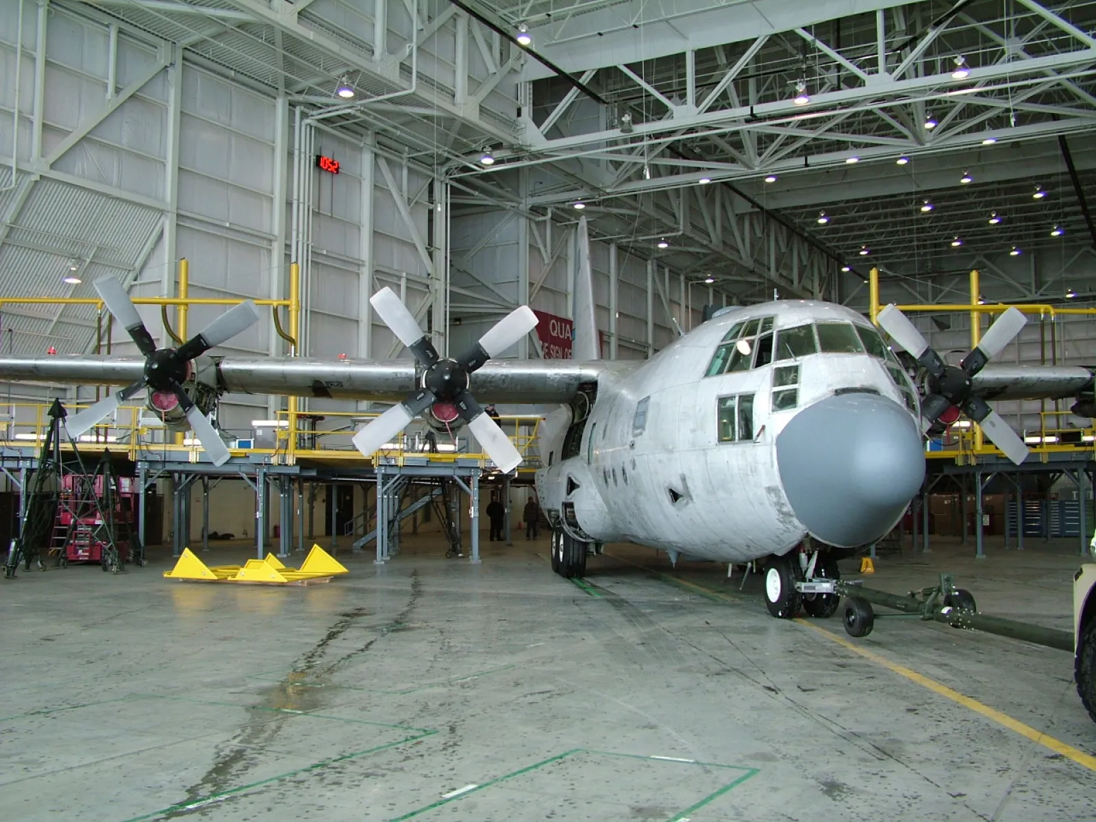 Large four-engine propeller airplane parked inside a spacious aircraft maintenance hangar with equipment around.