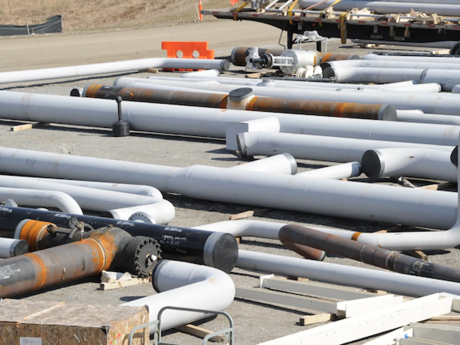 Large assortment of industrial metal pipes laid out on gravel at a construction or work site.