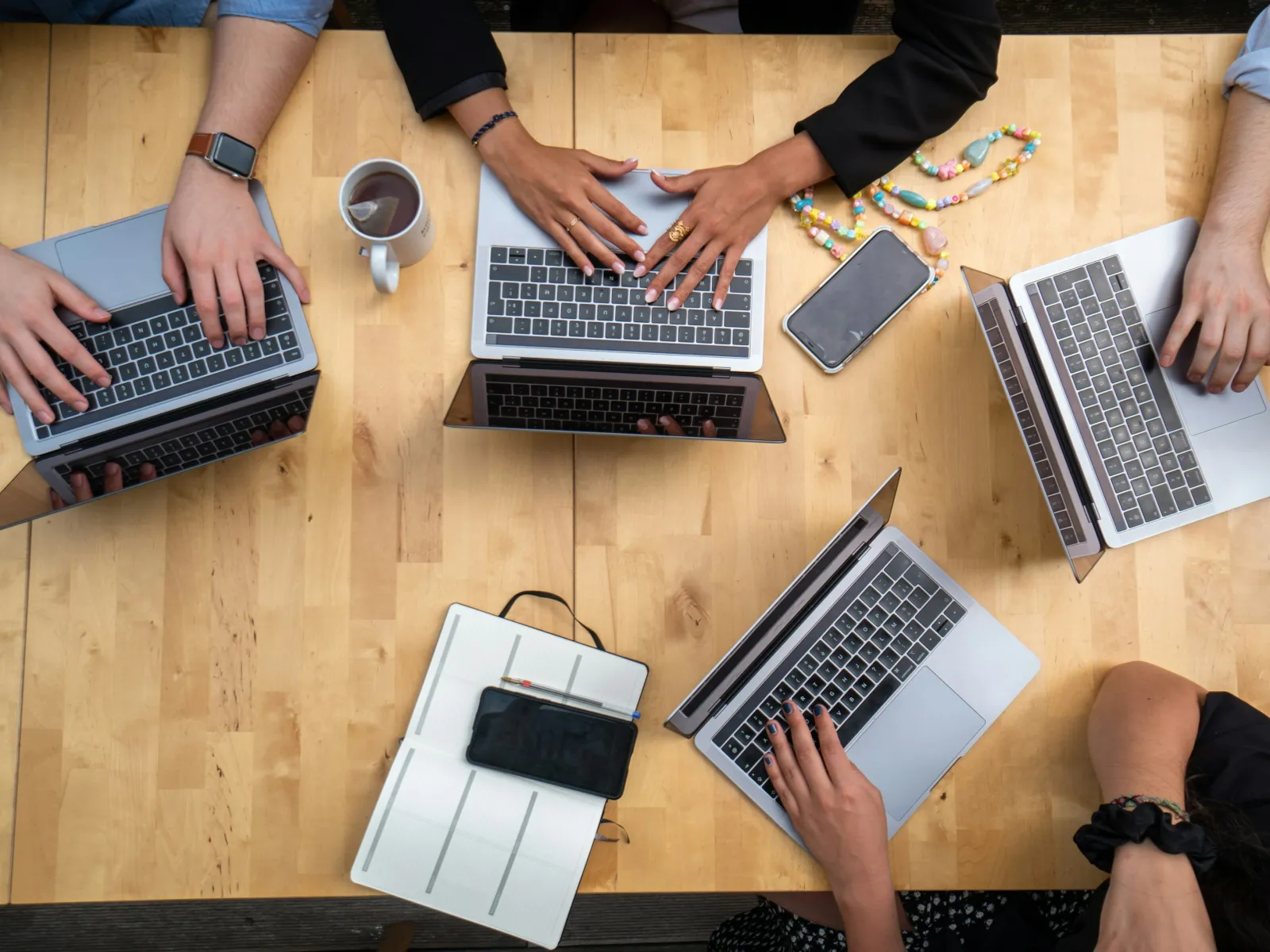 Overhead view of diverse people working on laptops at a wooden table with phones and coffee cup