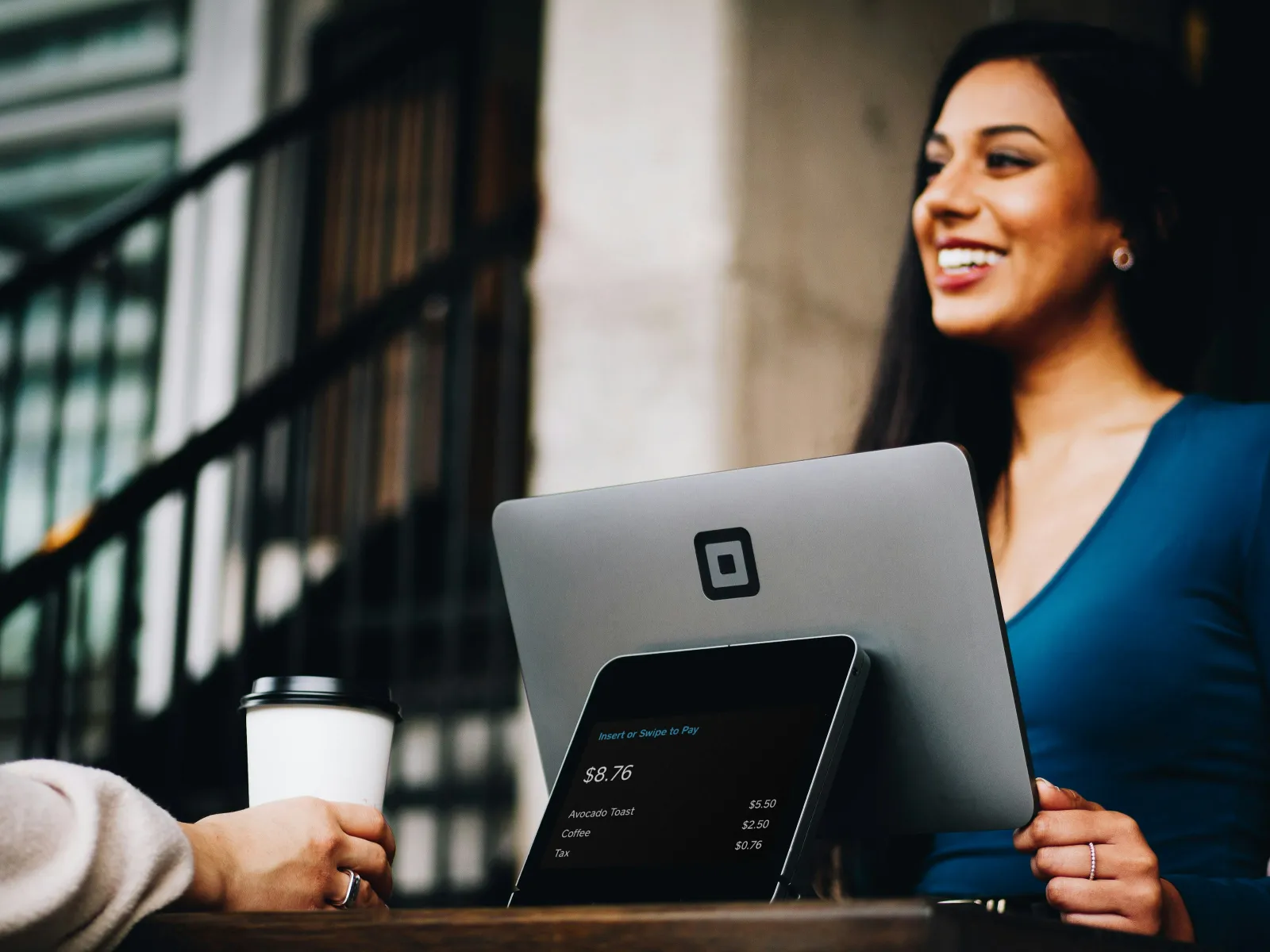 Smiling woman using a modern payment terminal to process a coffee purchase at a cafe counter.