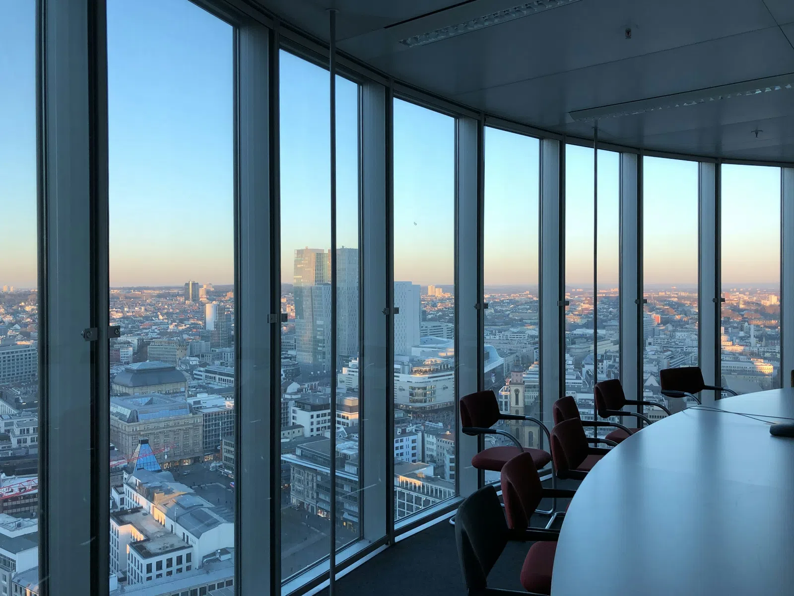 Panoramic view of a city skyline from a high-rise office meeting room with glass windows and chairs.