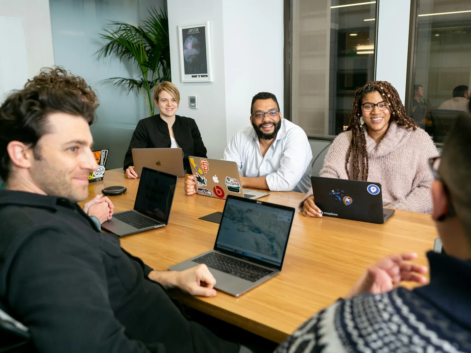 Diverse team of professionals in a meeting room collaborating with laptops around a wooden table.