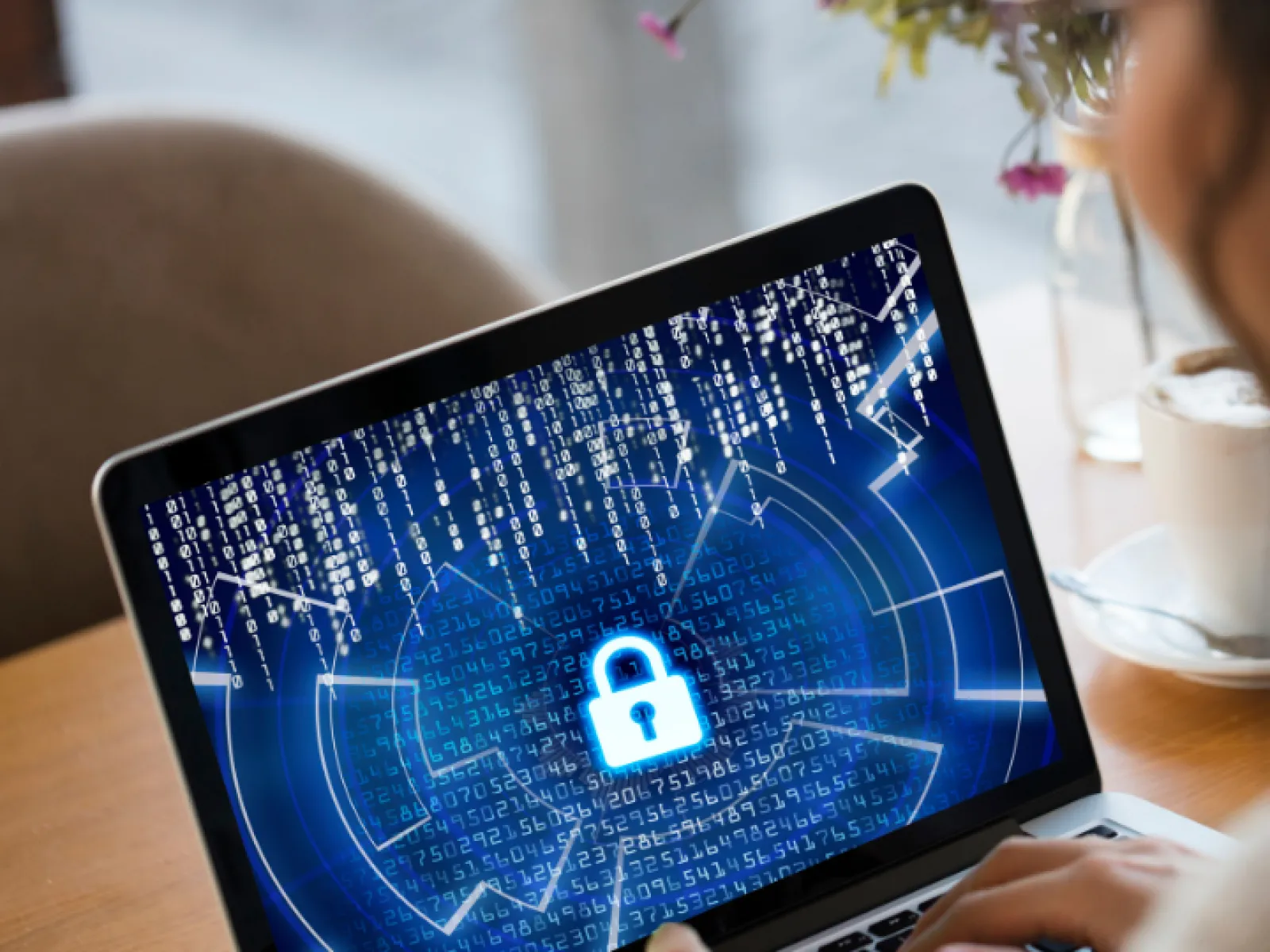 Person working on laptop with digital lock and encrypted data on screen symbolizing cybersecurity.
