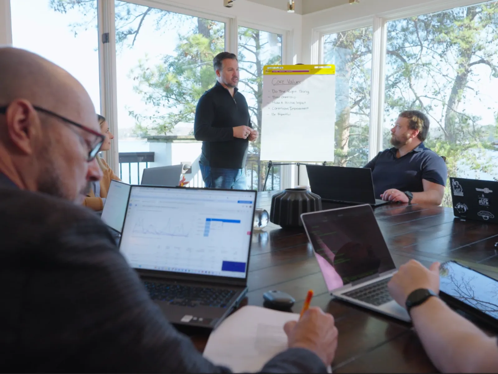 Team collaborating in a modern meeting room with laptops, a presenter, and a whiteboard.