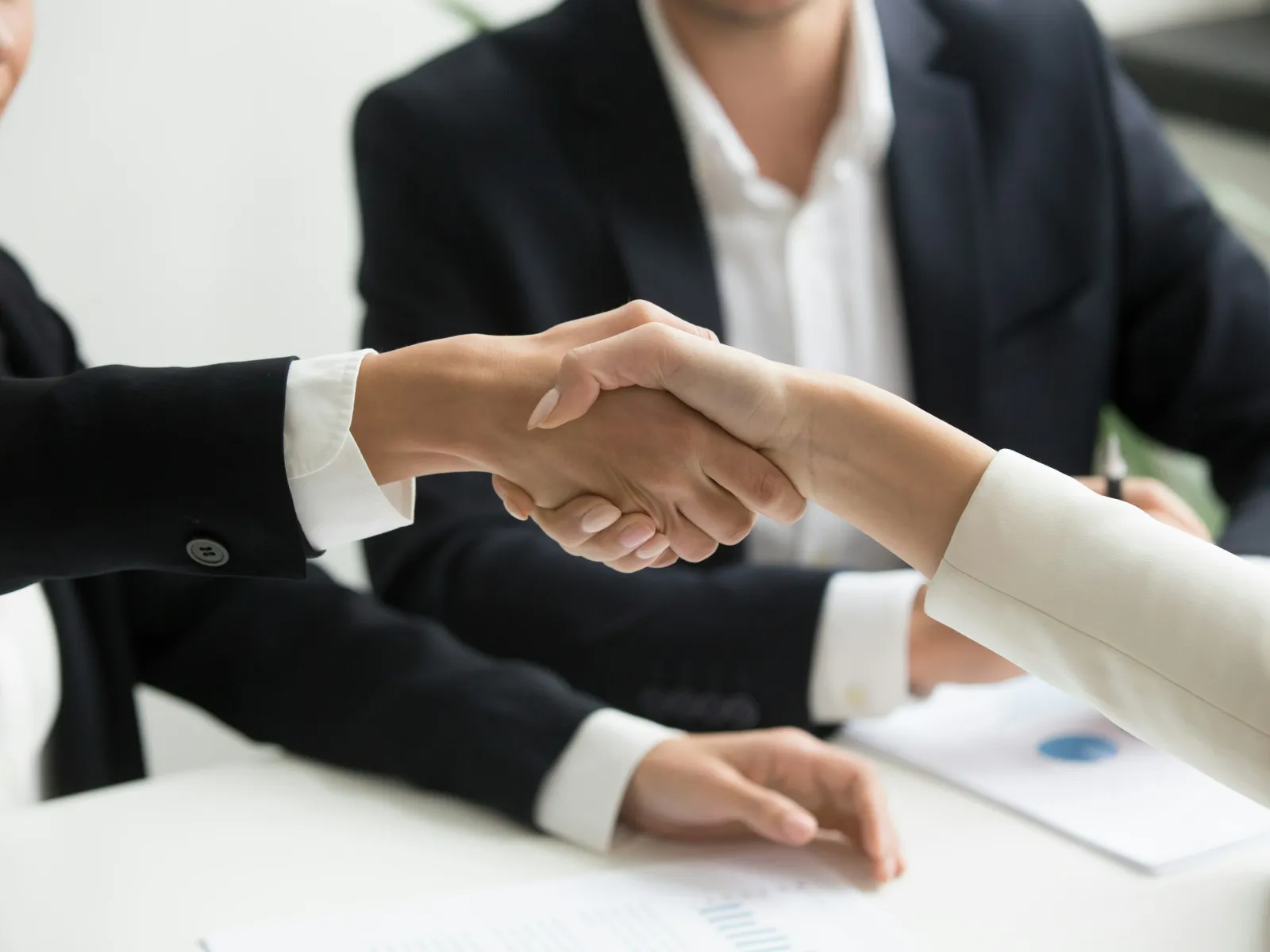 Two business professionals shaking hands over a desk with documents, symbolizing agreement or partnership.