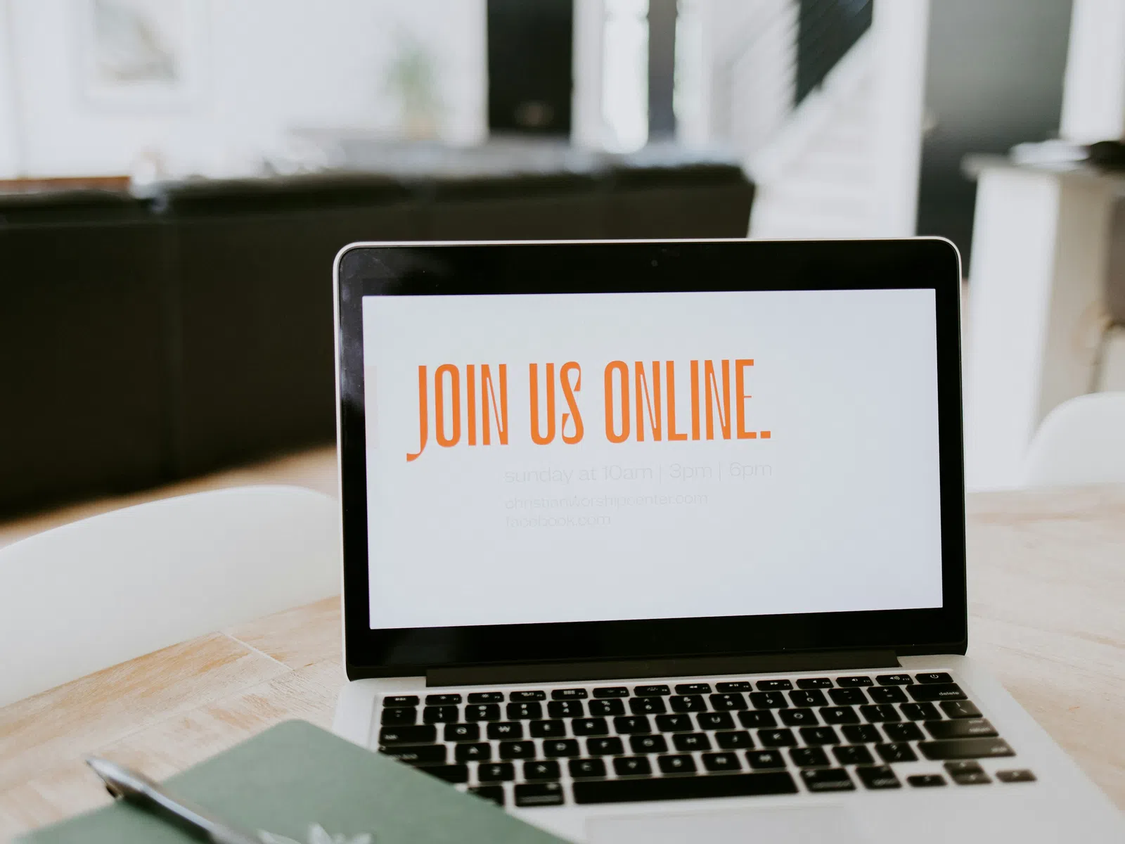 Laptop on wooden table displays Join Us Online message in orange text in a bright modern room.