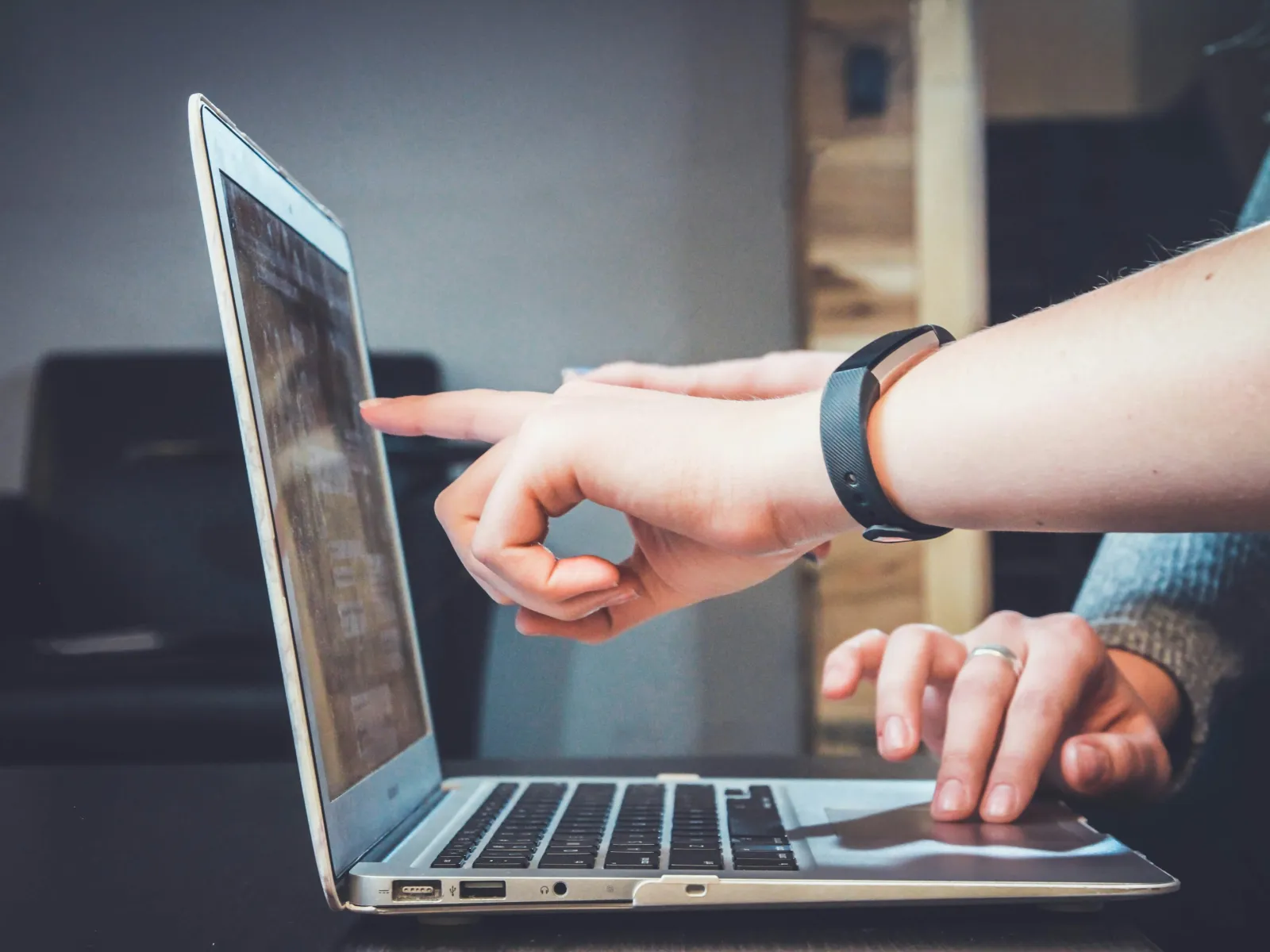 Person pointing at laptop screen while another types on keyboard in a casual indoor setting