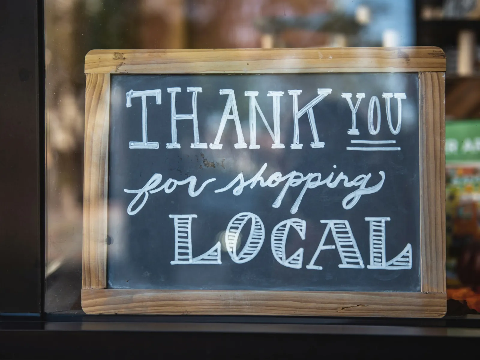 Chalkboard sign with wooden frame says Thank You for Shopping Local in white lettering.