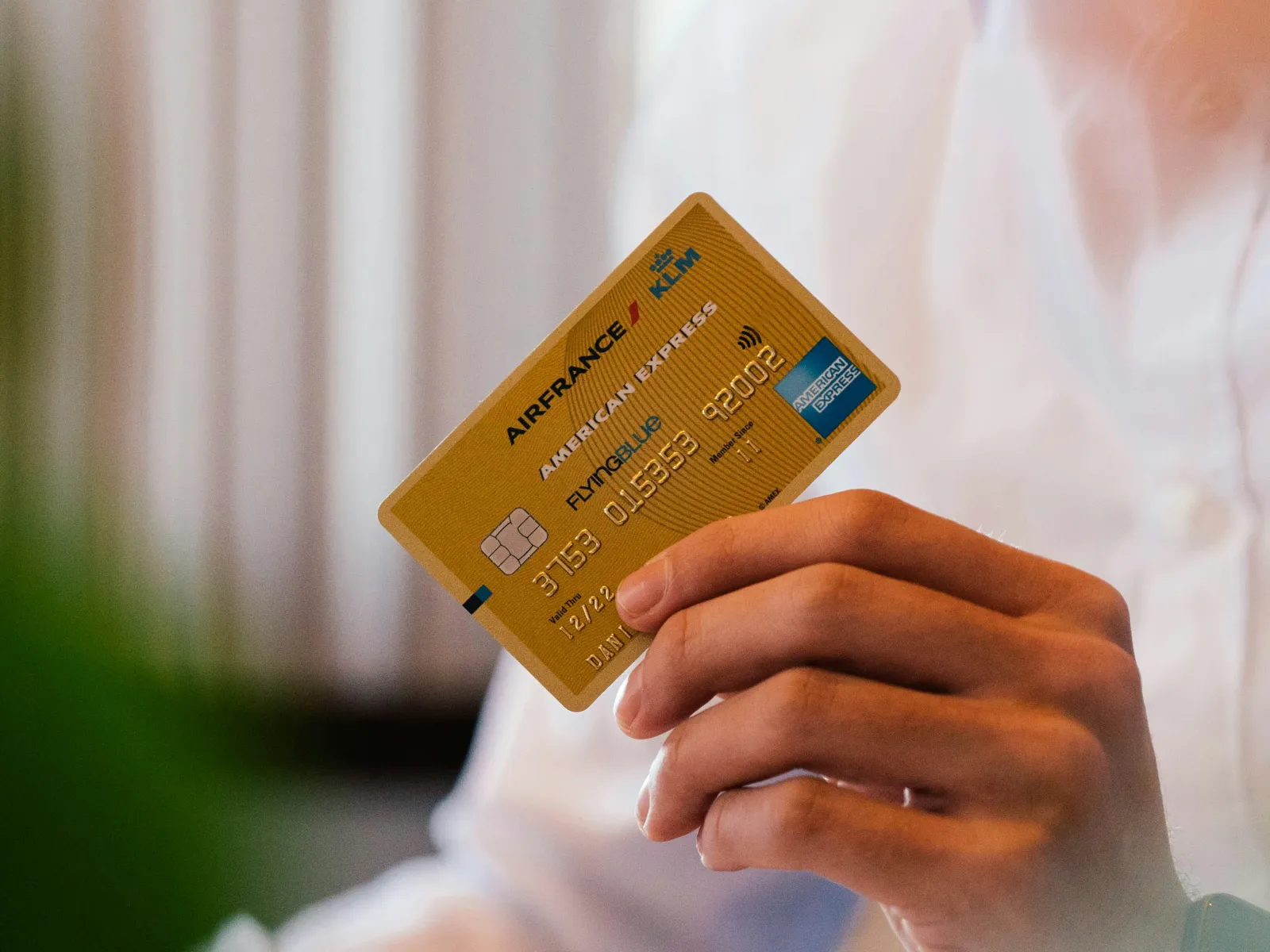 Person holding an Air France KLM American Express credit card in a light-colored shirt indoors.