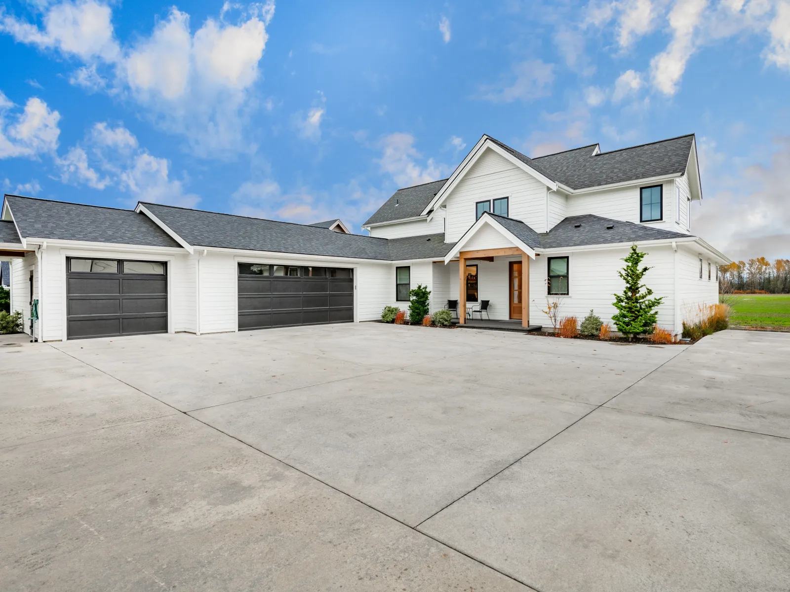 Modern white two-story house with large concrete driveway and triple garage under a blue cloudy sky.