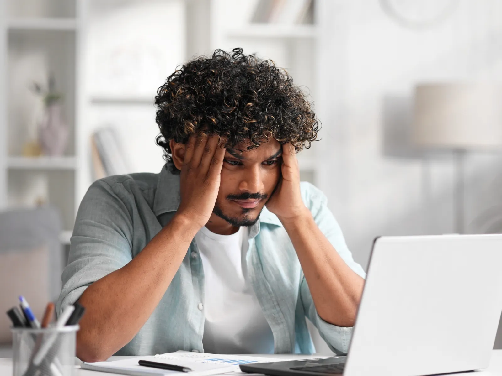 a person with the hand on the face looking at a laptop