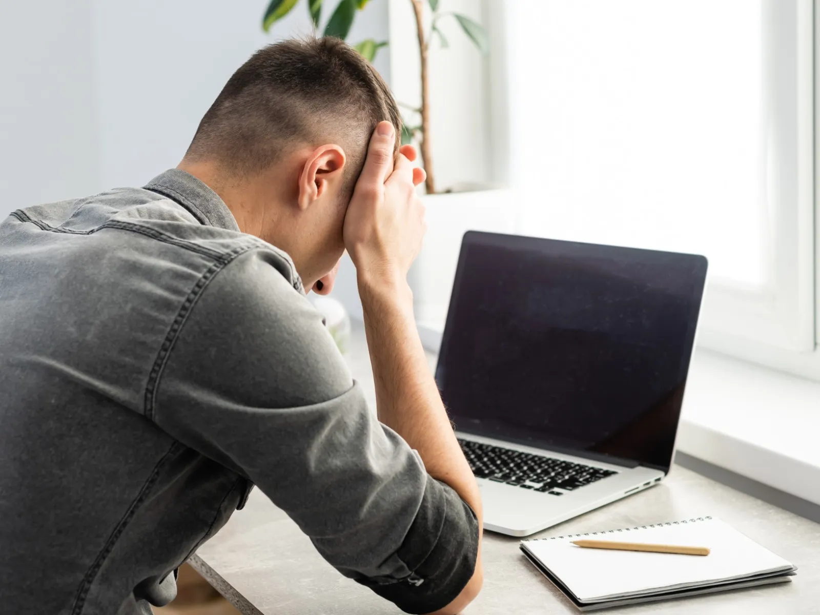 a person sitting at a desk with the head on the hand looking at a laptop