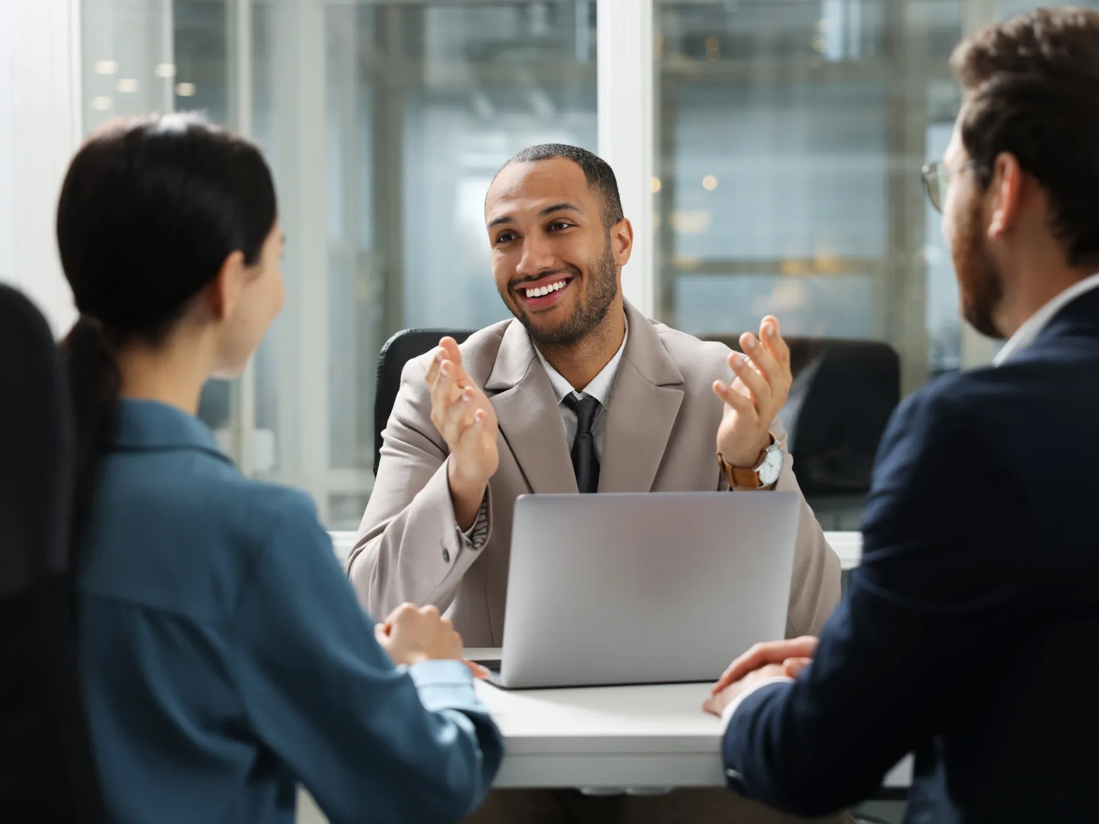 Businessman smiling and explaining something to colleagues during a meeting in modern office with laptop.