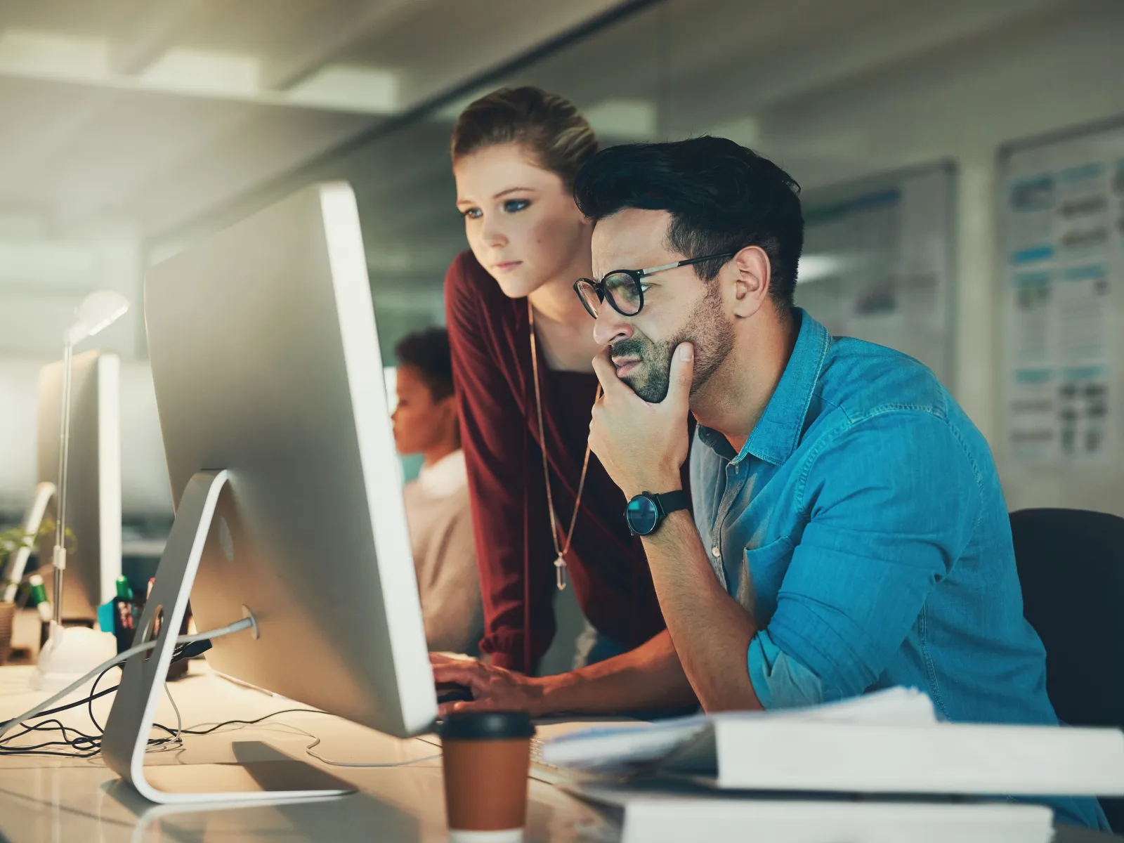 Two young professionals focused on a desktop computer in a modern office working late together