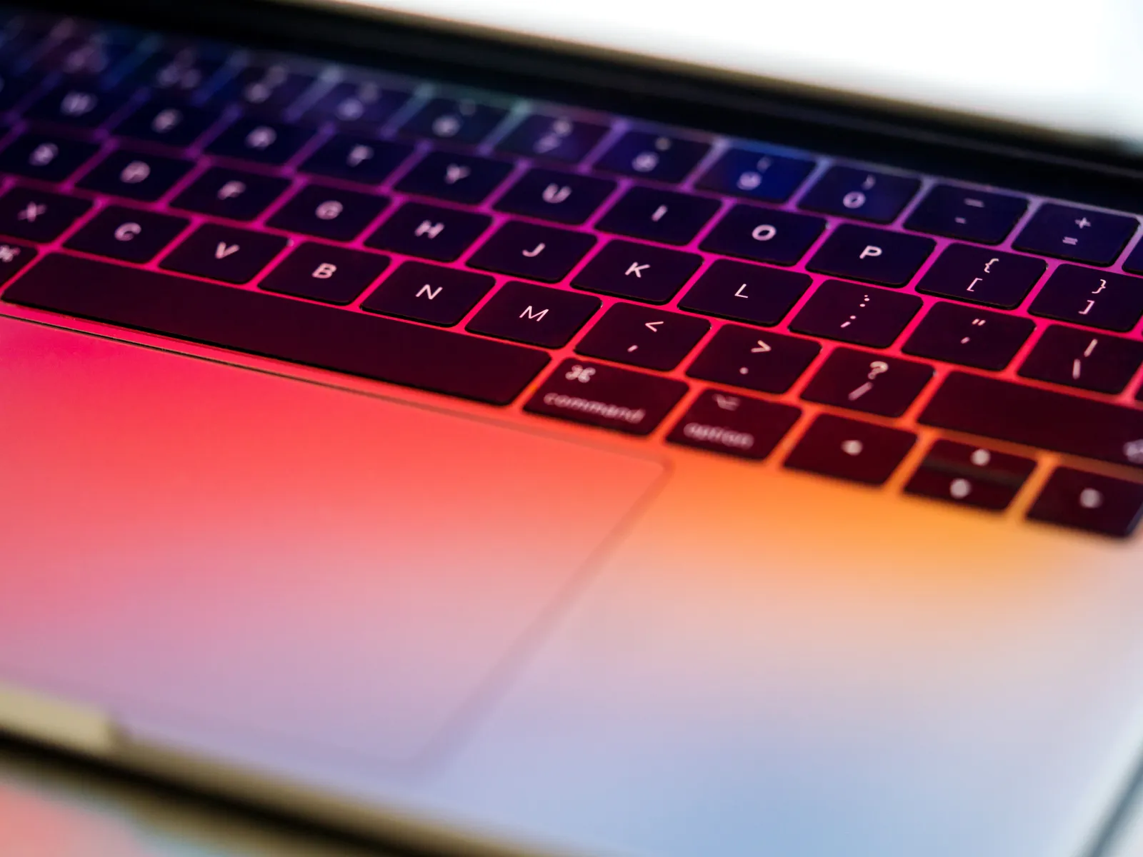 Close-up of a laptop keyboard illuminated with colorful pink and orange gradient lighting.