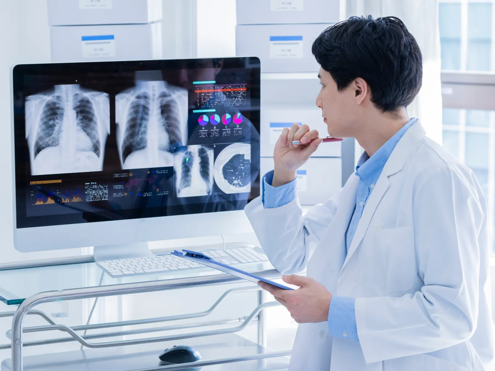 Doctor analyzing digital chest X-rays and medical charts on a computer screen in a modern clinic room.