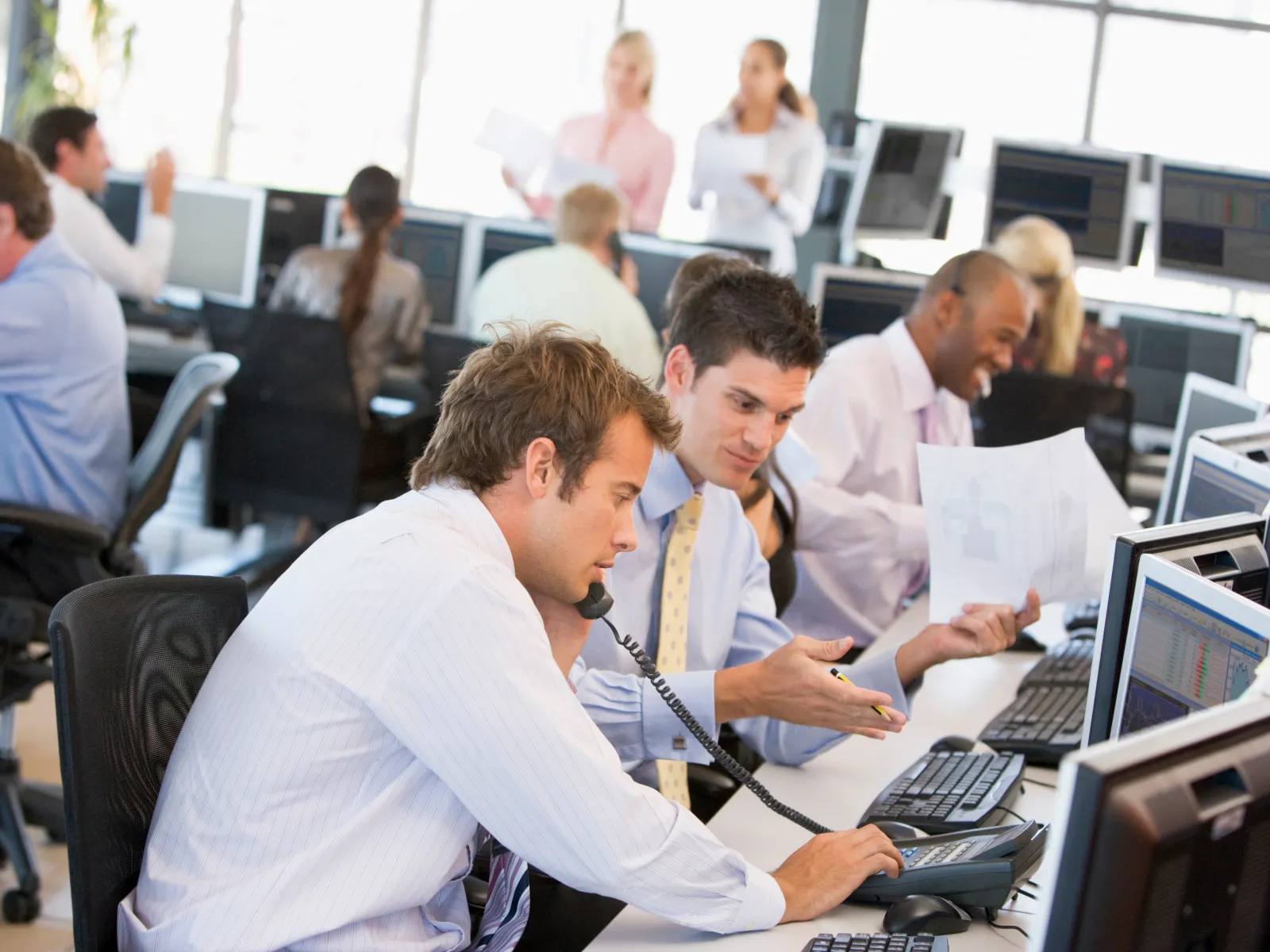Professionals working collaboratively at desks with computers and phones in a busy modern office setting