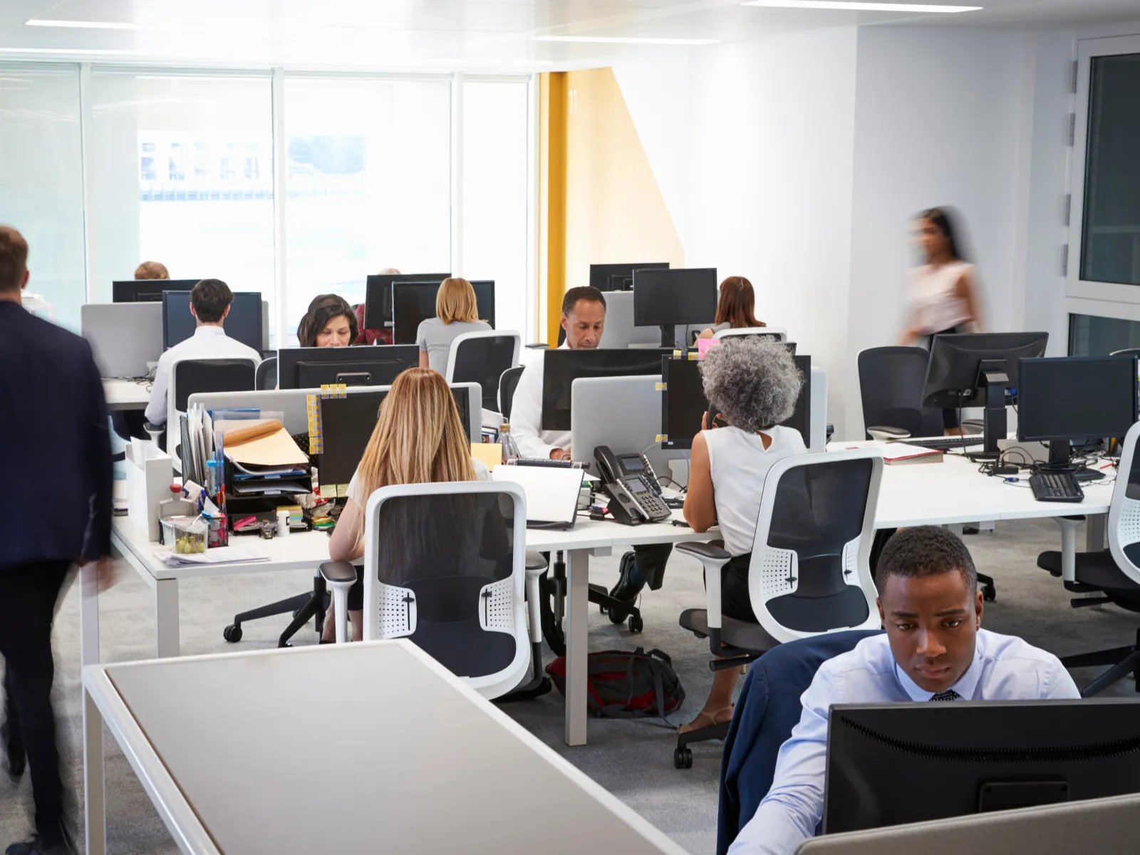 Busy modern office with diverse employees working at desks with computers and office supplies.