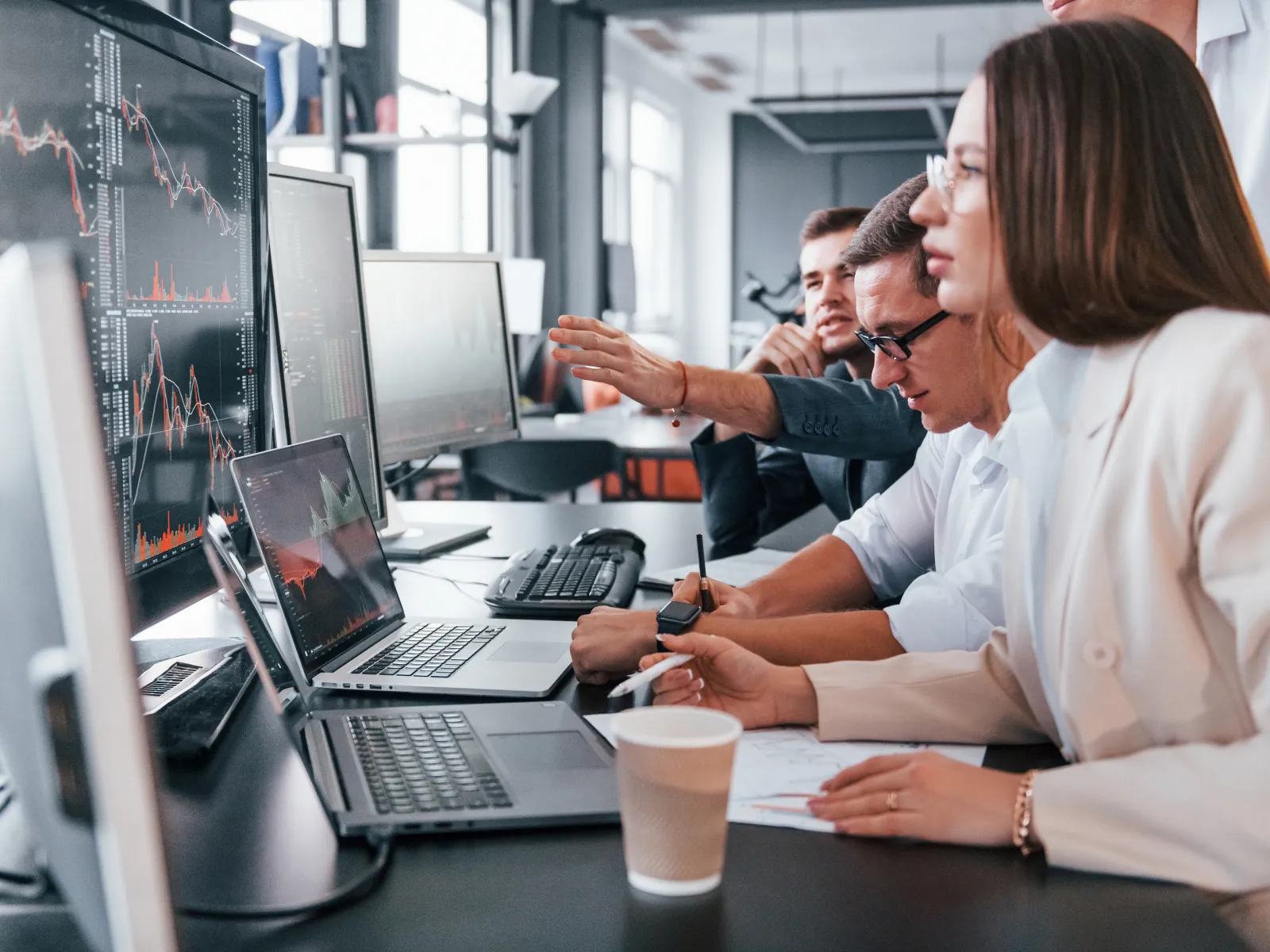 Group of business professionals analyzing financial data on multiple screens in a modern office setting