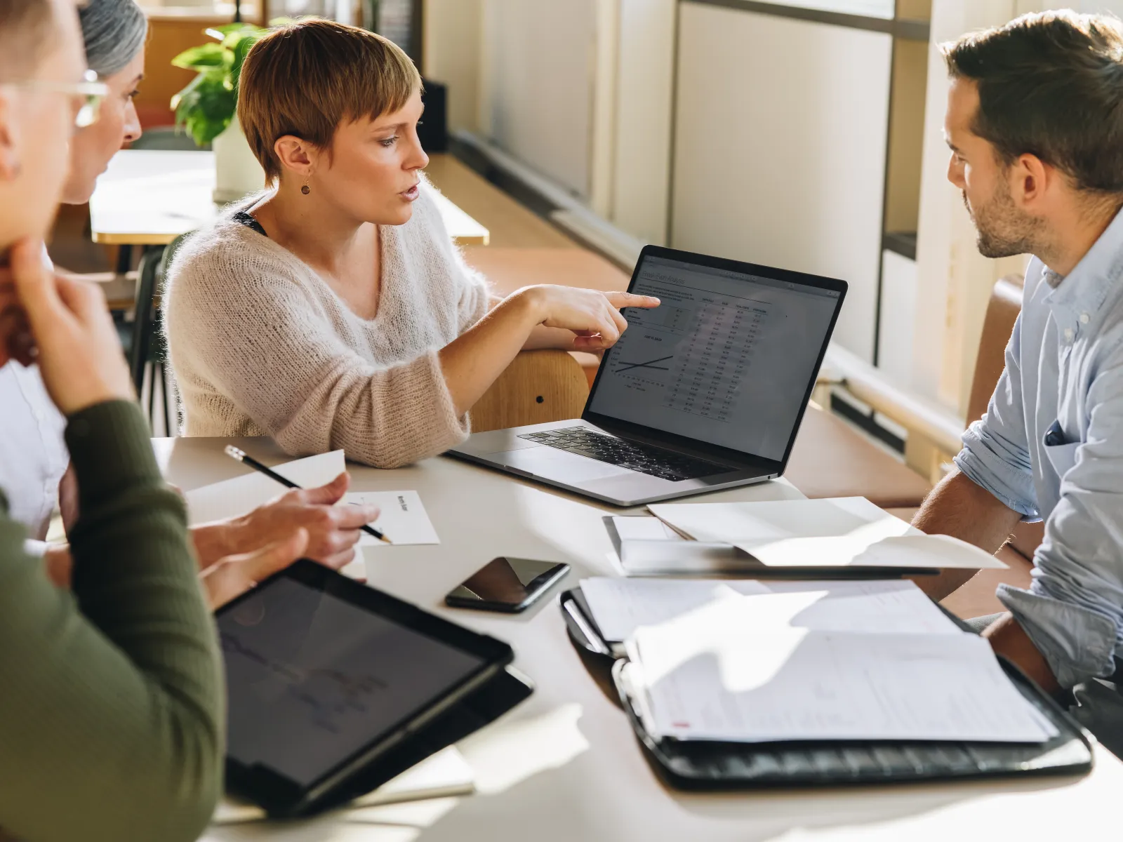 Young professionals discussing data on laptop during a bright collaborative office meeting.